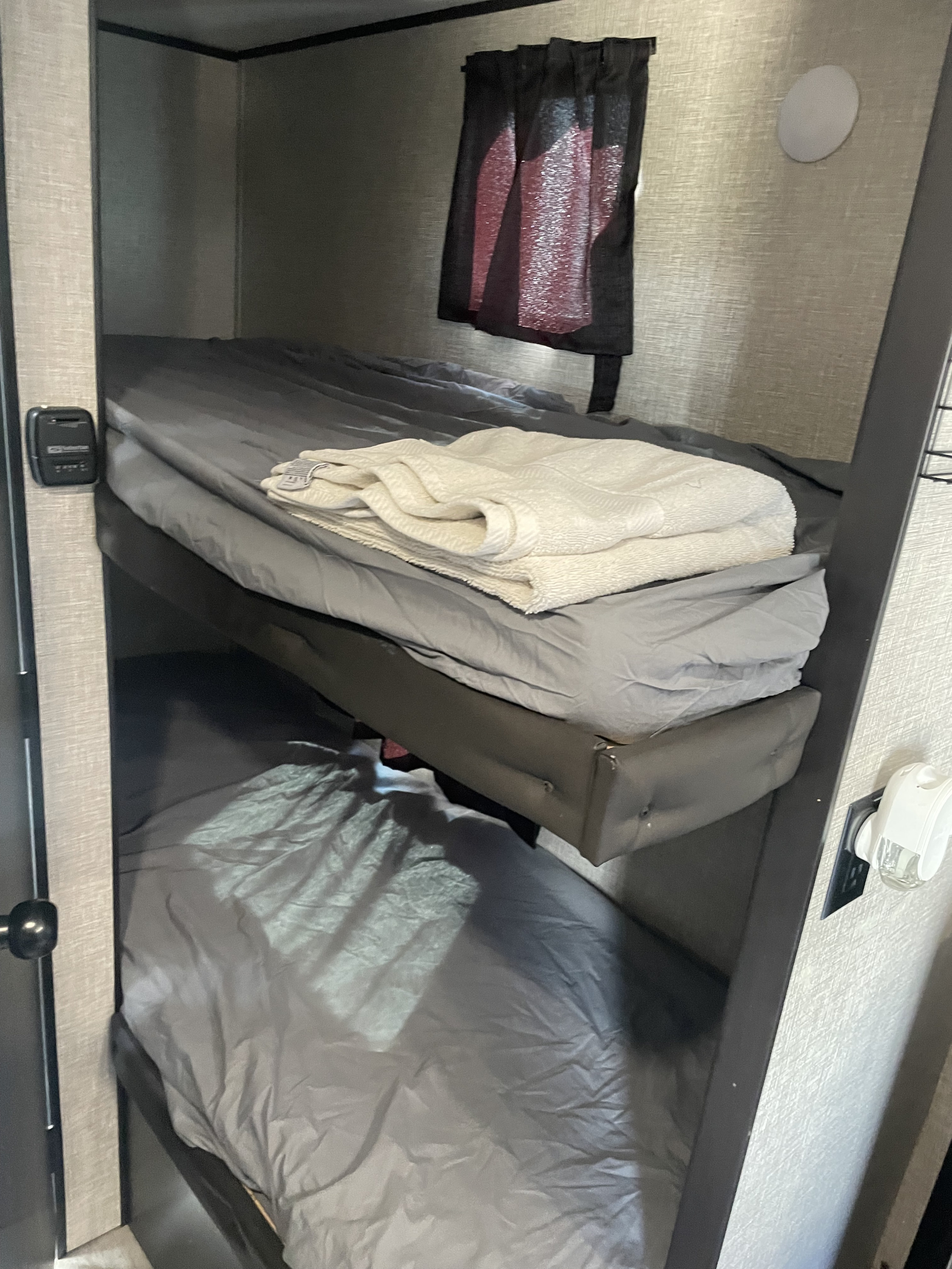 Compact RV rental interior featuring two bunk beds with grey sheets. A white towel is neatly folded on the top bunk.. Jayco Jay Feather 2021