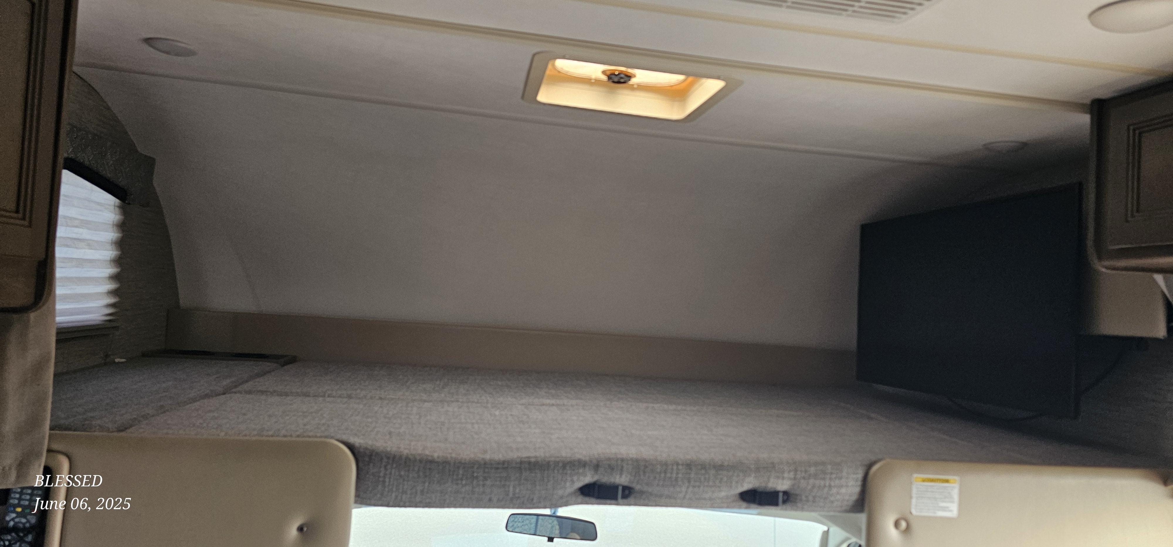Inside an RV rental: the cab-over sleeping area features a grey mattress, window, and TV. A ceiling vent above.. Thor Chateau 2022