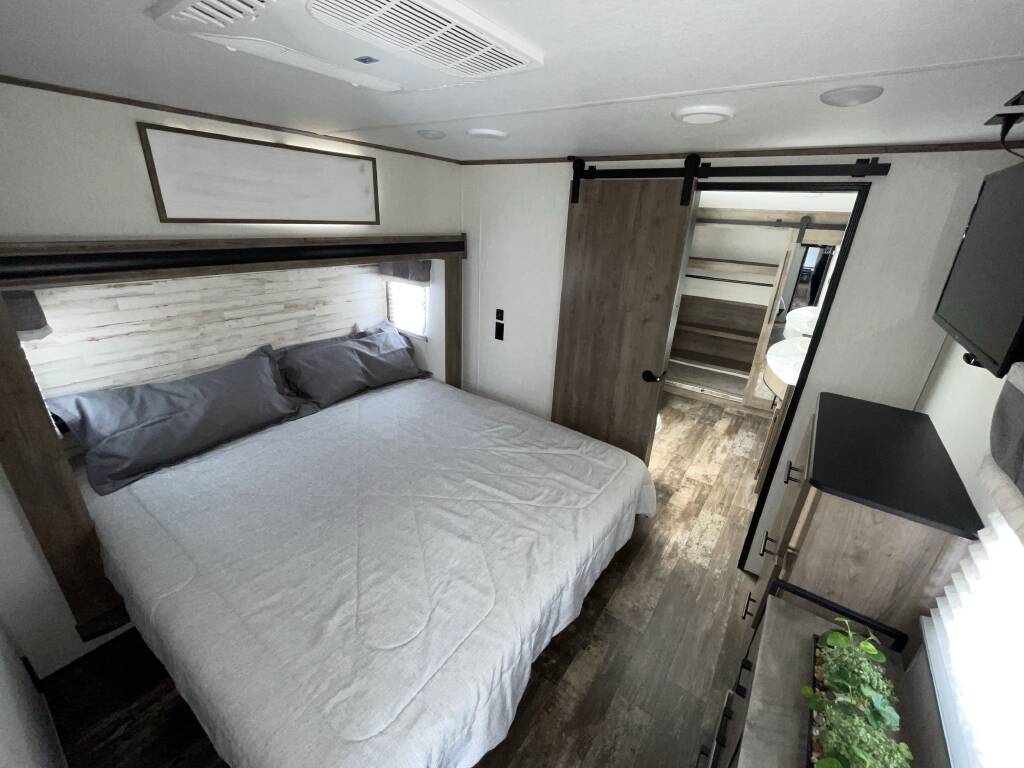Modern RV rental bedroom with a comfy bed, barn door access to bathroom, and TV. Perfect for your next trip!. Forest River Sabre 2021