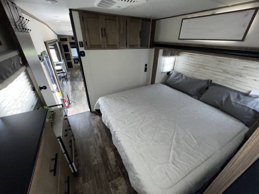 Inside an RV rental, discover a comfortable bedroom with a large bed, wood headboard, upper cabinets, and a dresser.. Forest River Sabre 2021