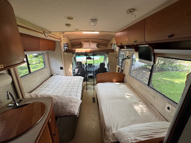 Spacious RV rental interior featuring two comfortable beds, a mini-kitchen, and overhead storage. Ideal for road trips.. Itasca Navion 2006