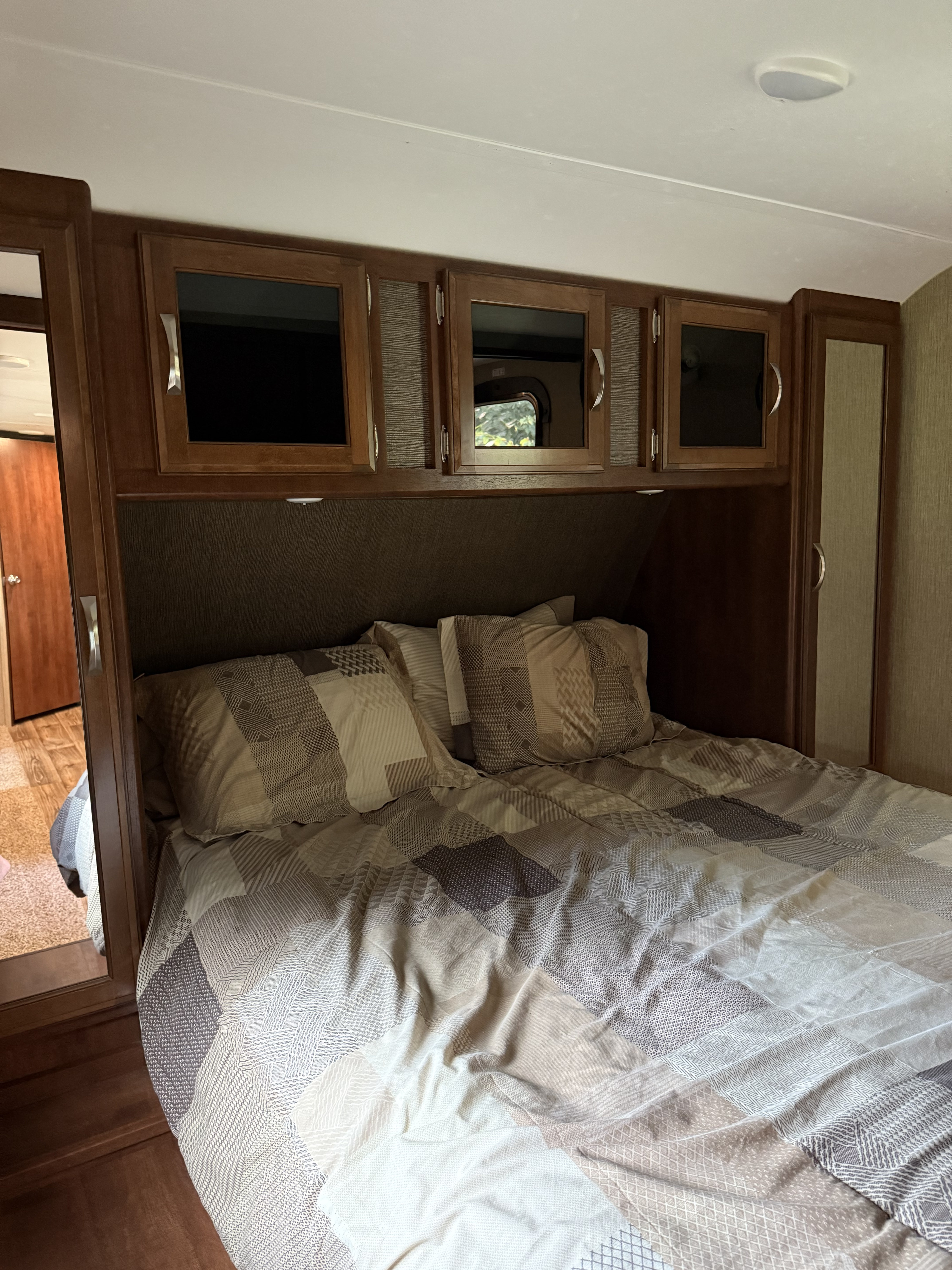 Interior of an RV rental bedroom with a neatly made bed, overhead storage, and integrated wood cabinetry, offering cozy compact living.. Keystone RV Passport Grand Touring 2017