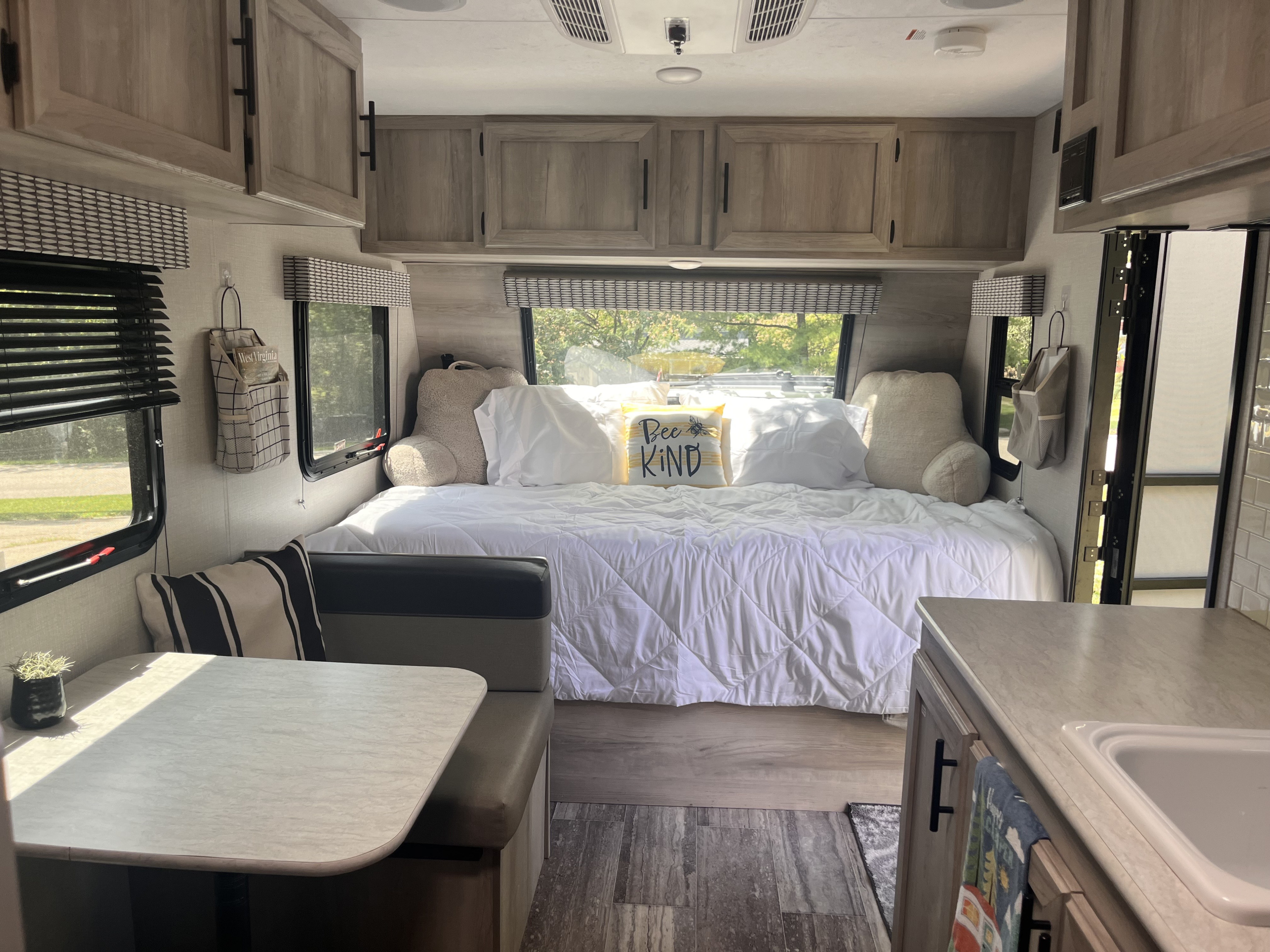Bright and modern RV rental interior featuring a cozy bedroom, dinette, and compact kitchen area.. Sportsmen Classic 2021