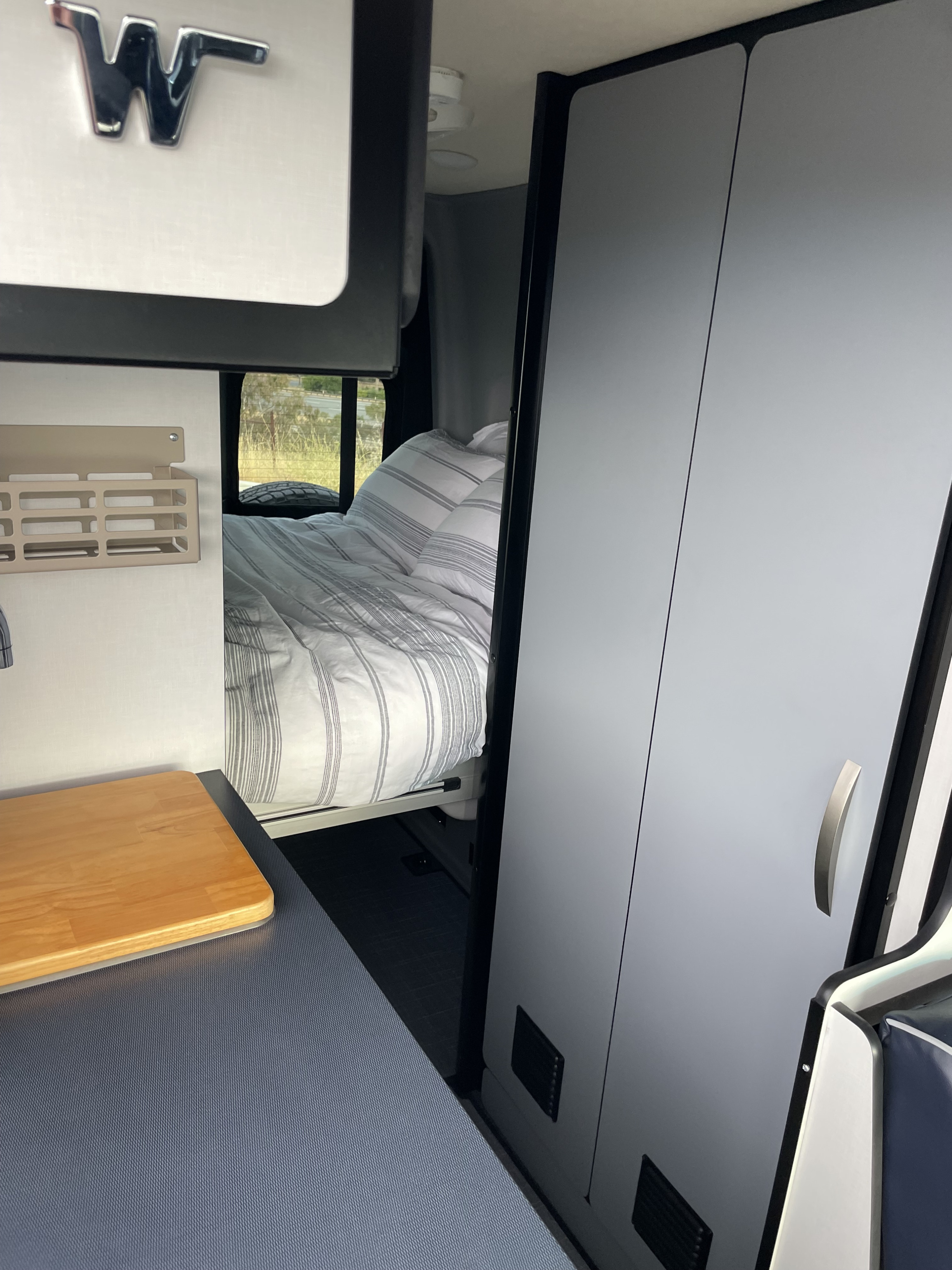 Winnebago rv rental interior: a comfy bed, kitchenette with wood counter, and sleek storage cabinets.. Winnebago Revel 2023