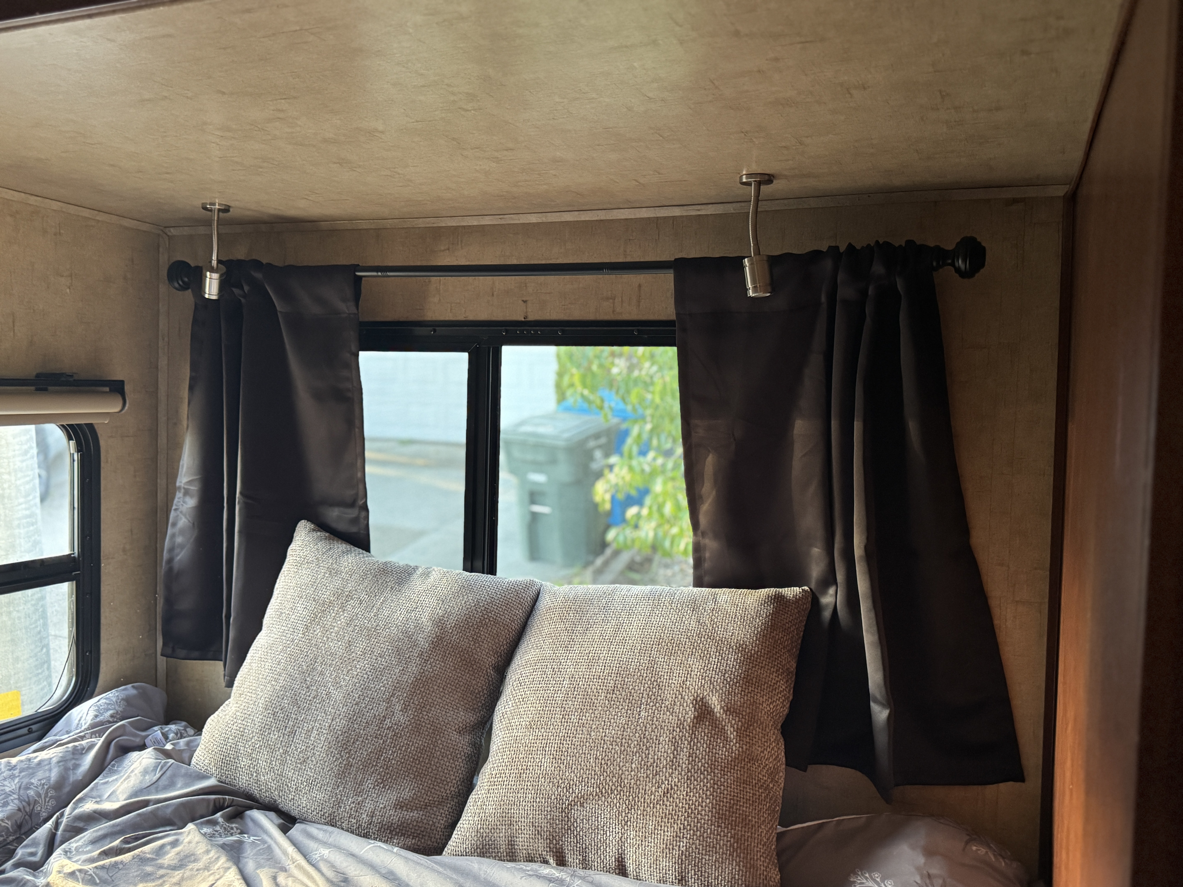 Cozy RV rental bedroom with gooseneck lights, dark curtains, and comfortable bedding by the window.. Forest River Sunseeker MBS 2016