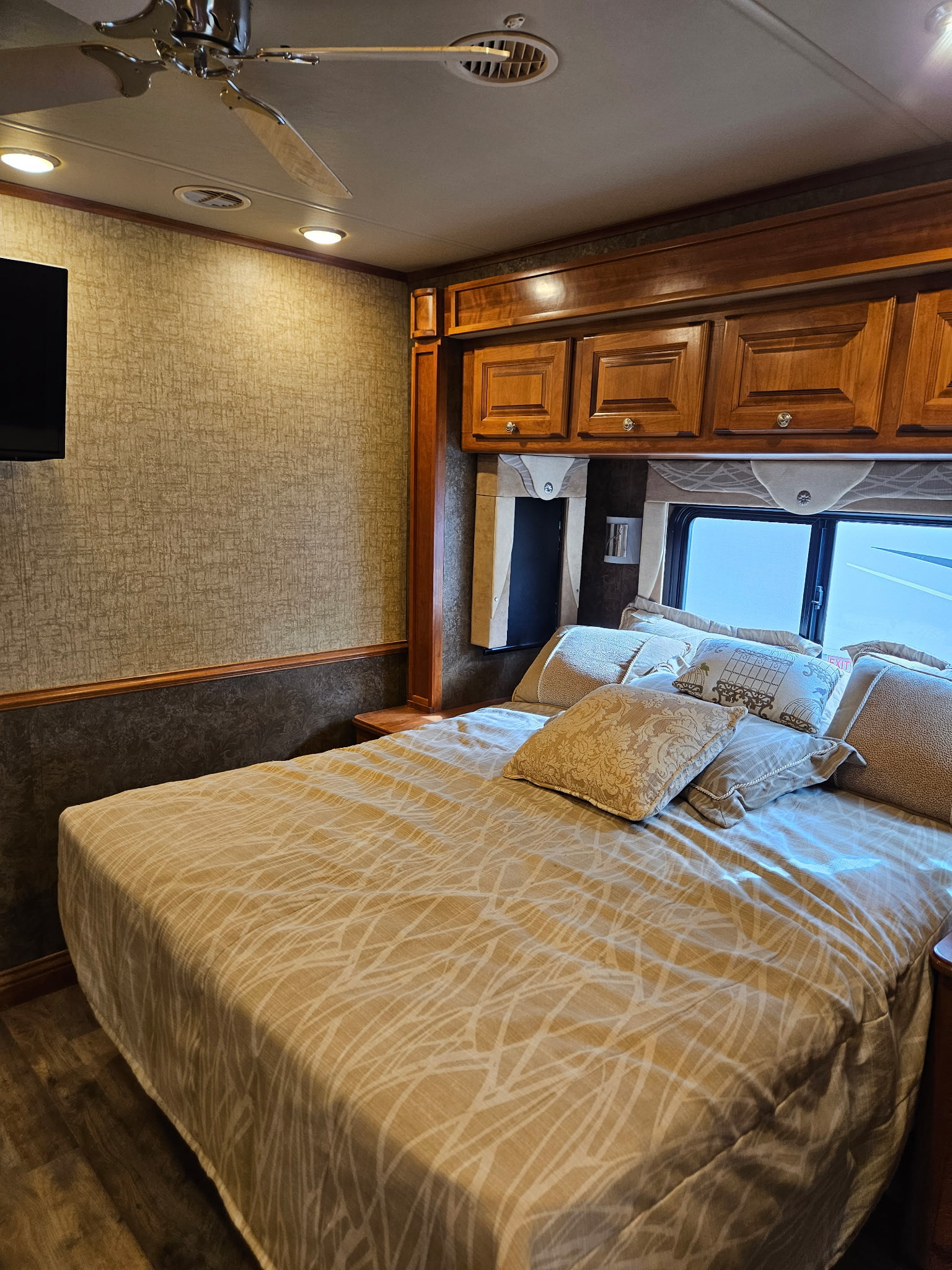 Cozy RV rental bedroom with a comfortable bed, textured walls, overhead cabinets, TV, and ceiling fan for a relaxing stay.. Allegro Allegro Motorhome 2015