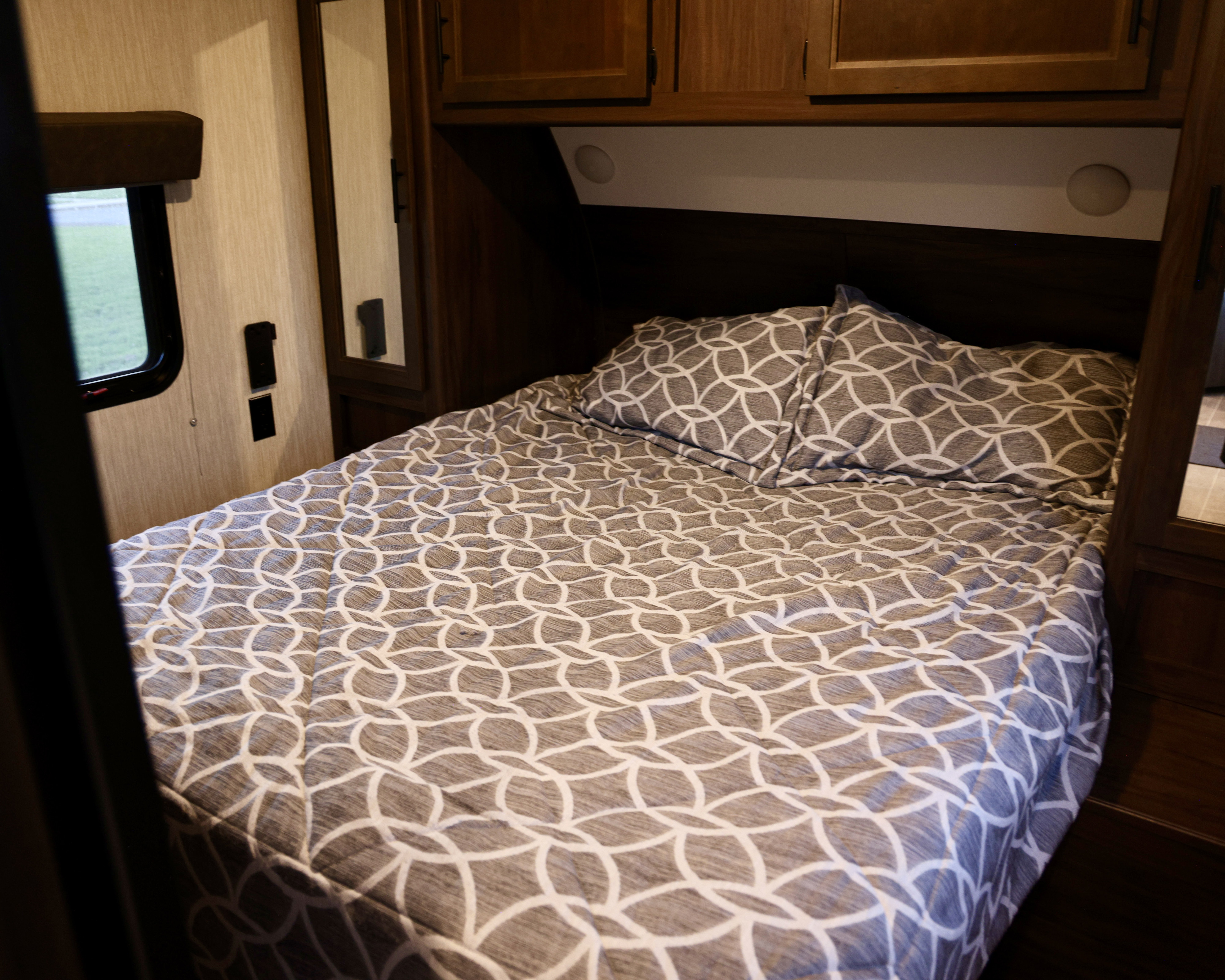 Cozy RV rental bedroom with a comfy bed, patterned bedding, and wooden cabinets, perfect for a relaxing getaway.. Forest River Cherokee 2020
