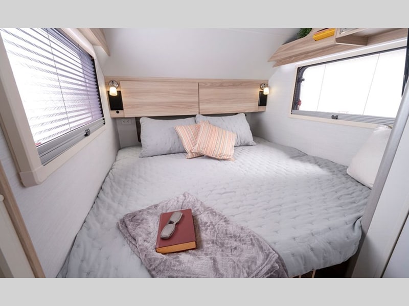 Inside a cozy rv rental bedroom featuring a spacious bed, natural light from windows, and integrated headboard lighting.. nuCamp T@B 2021