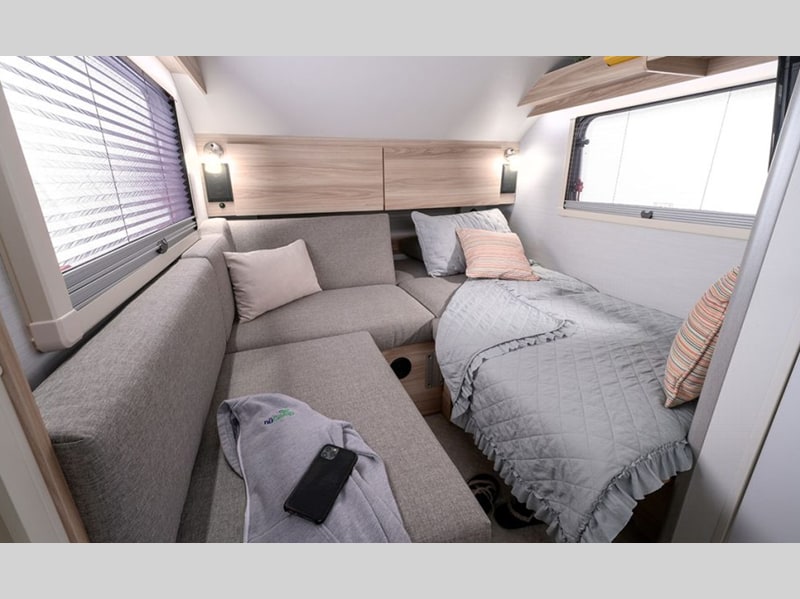 Compact RV rental interior: a comfy grey sofa, single bed with quilted blanket, and bright windows create a cozy living space.. nuCamp T@B 2021