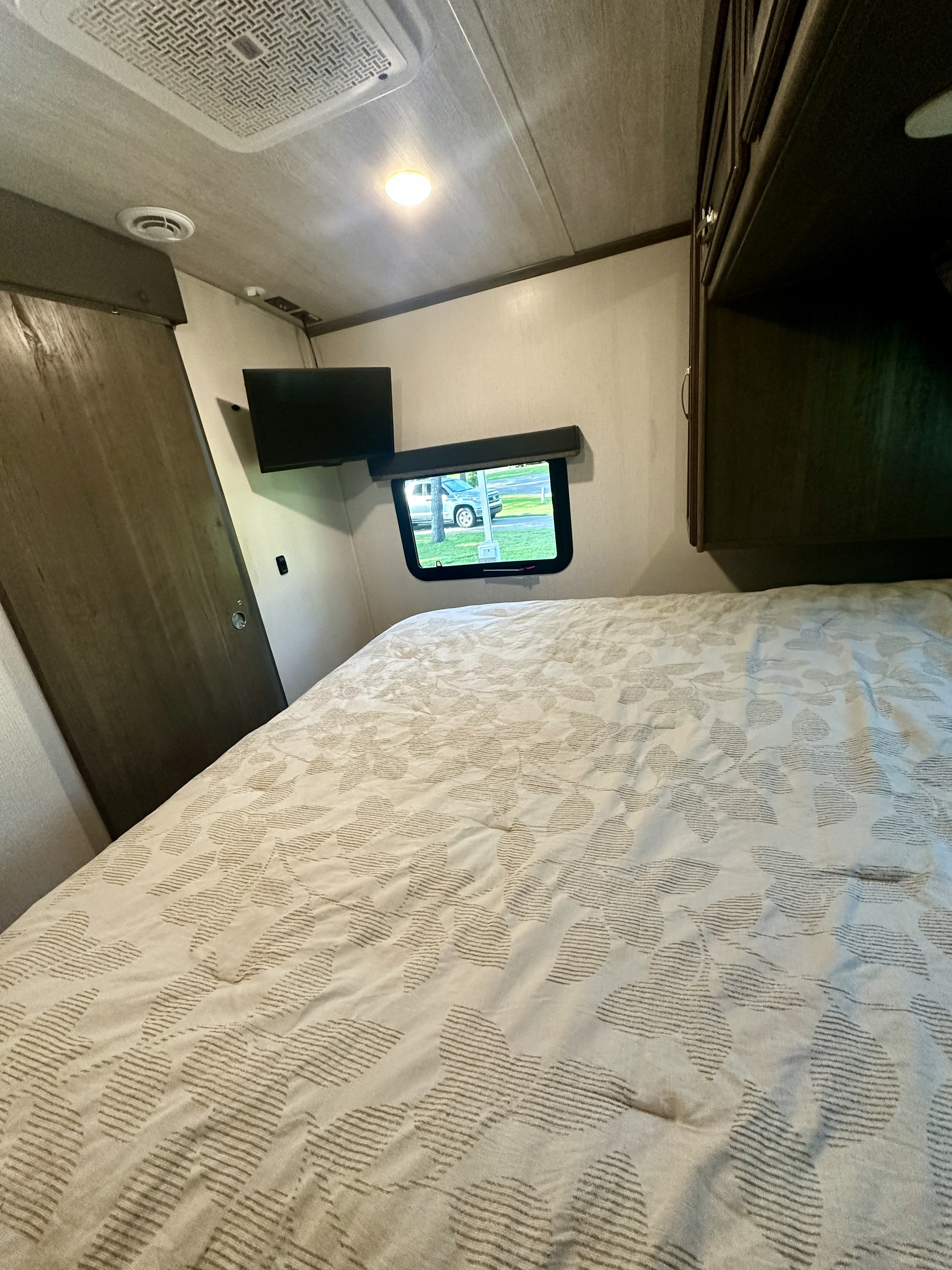 Cozy rv rental bedroom features: patterned bed, window with car view, wall-mounted TV, and storage.. Keystone RV Cougar 2023