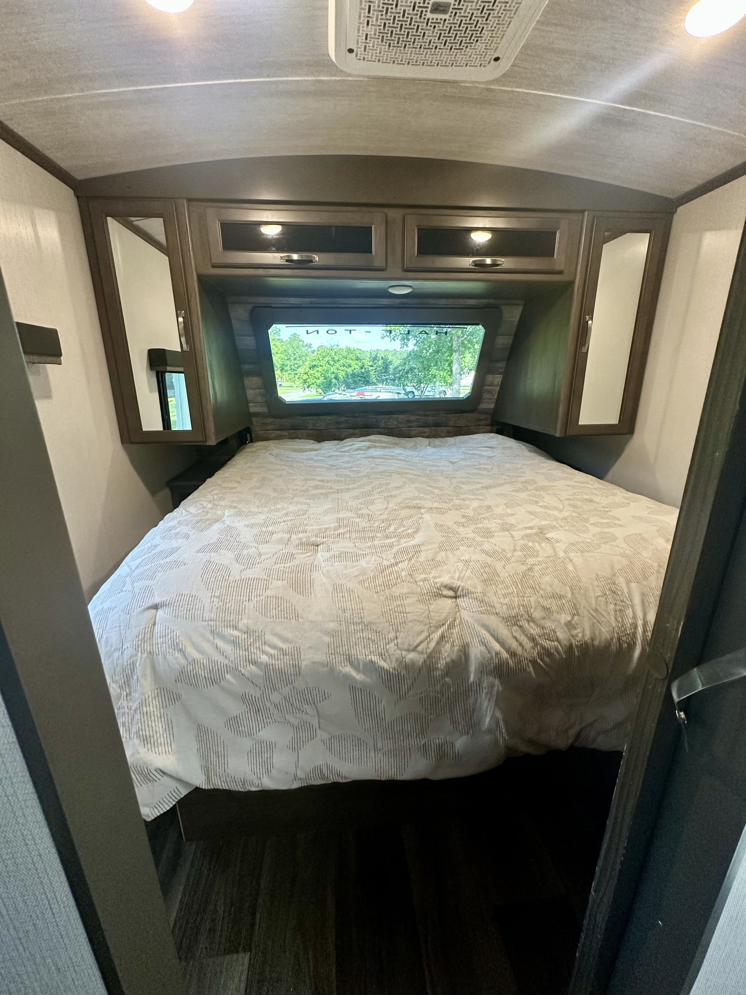 Inviting RV rental bedroom with a comfy bed, overhead compartments, and a serene outdoor view from the back window.. Keystone RV Cougar 2023