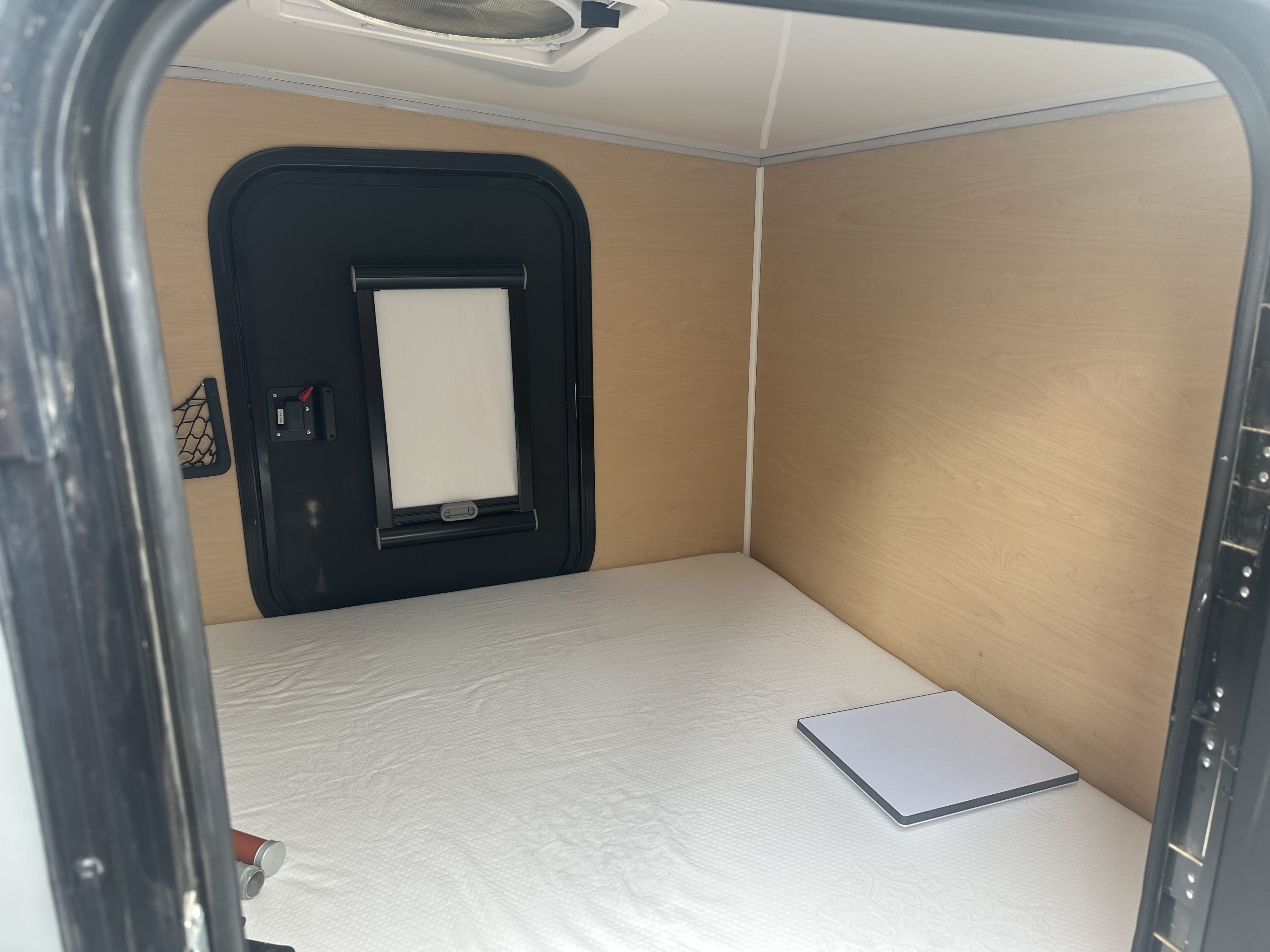 Cozy RV rental interior: a white mattress, wood walls, window, mesh net, and a small table.. Boreas XT 2022