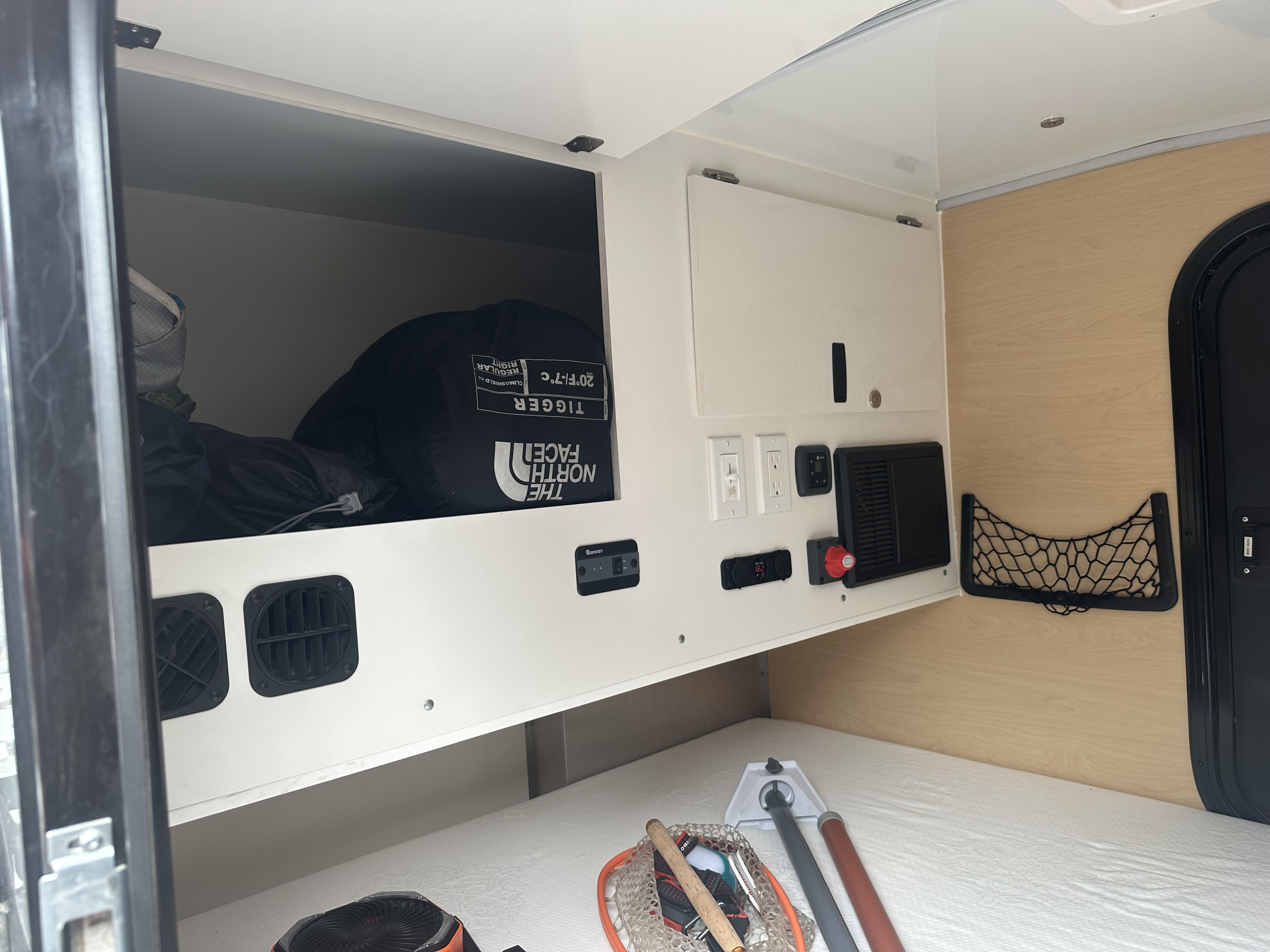 Experience a compact RV rental. Interior shows a bed, overhead storage with camping gear, and essential electrical controls.. Boreas XT 2022