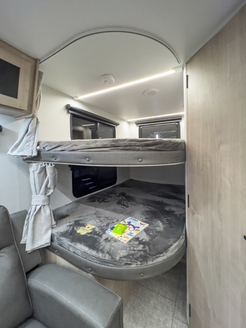 RV rental interior: modern bunk beds with soft gray bedding, a comfy armchair, and bright LED lighting in a cozy space.. Grand Design Imagine XLS 2025