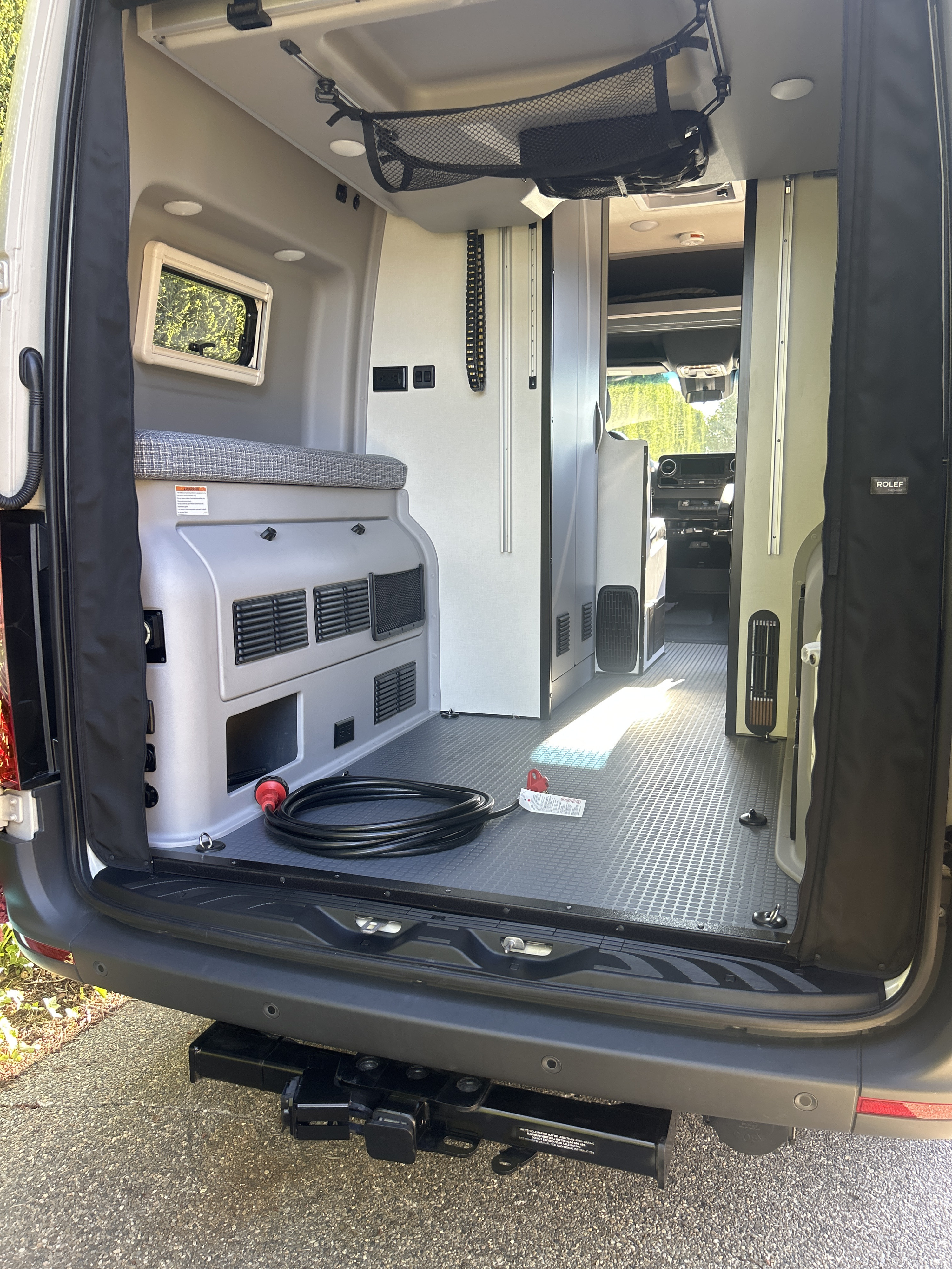 Explore this RV rental's versatile camper van interior, featuring durable flooring, bed, and ample storage from the rear.. Winnebago Revel 2023