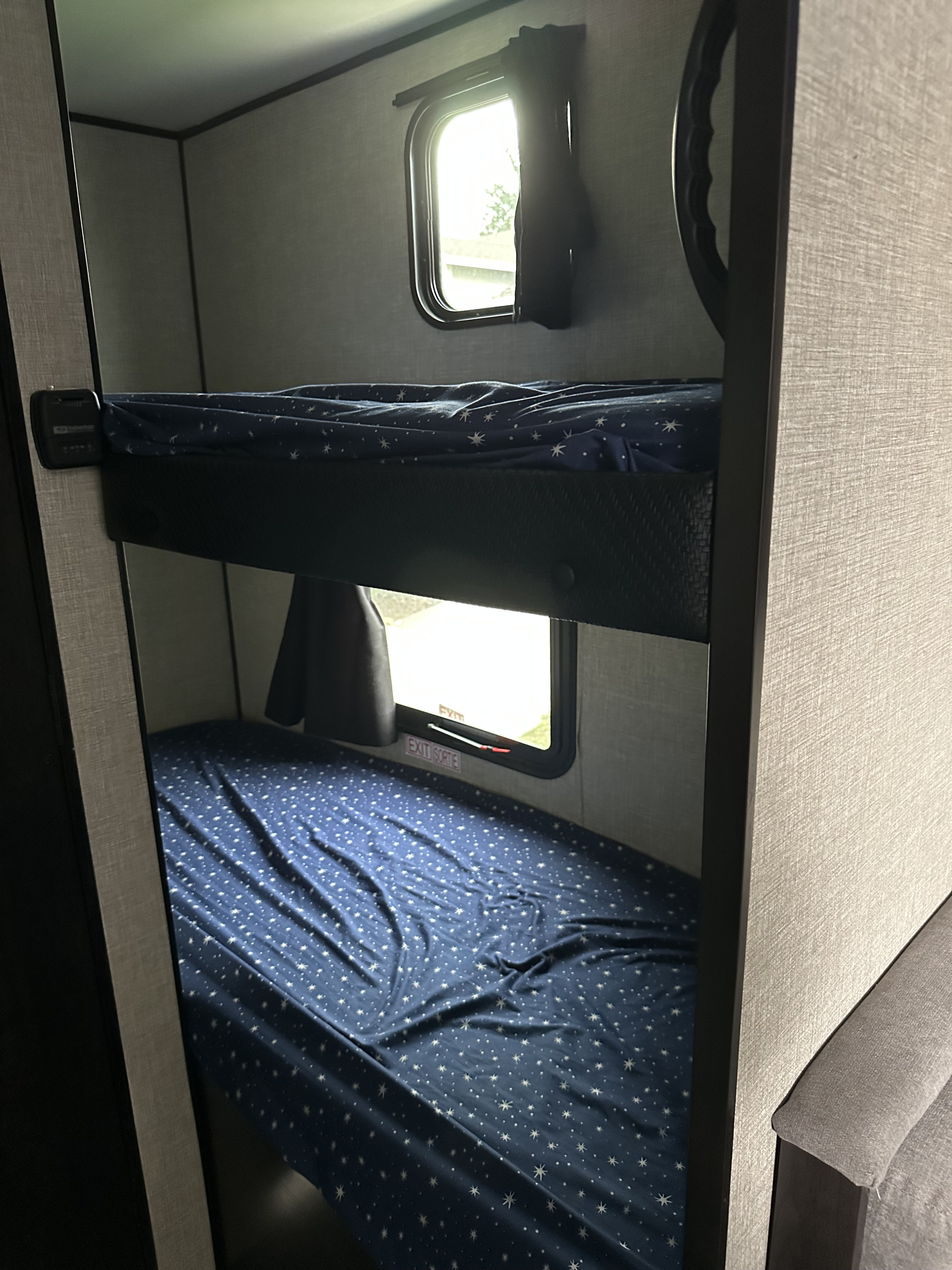 Bright interior of an RV rental showing a double bunk bed setup with starry blue sheets and sunlit windows.. Jayco Jay Flight SLX Baja Edition 2021