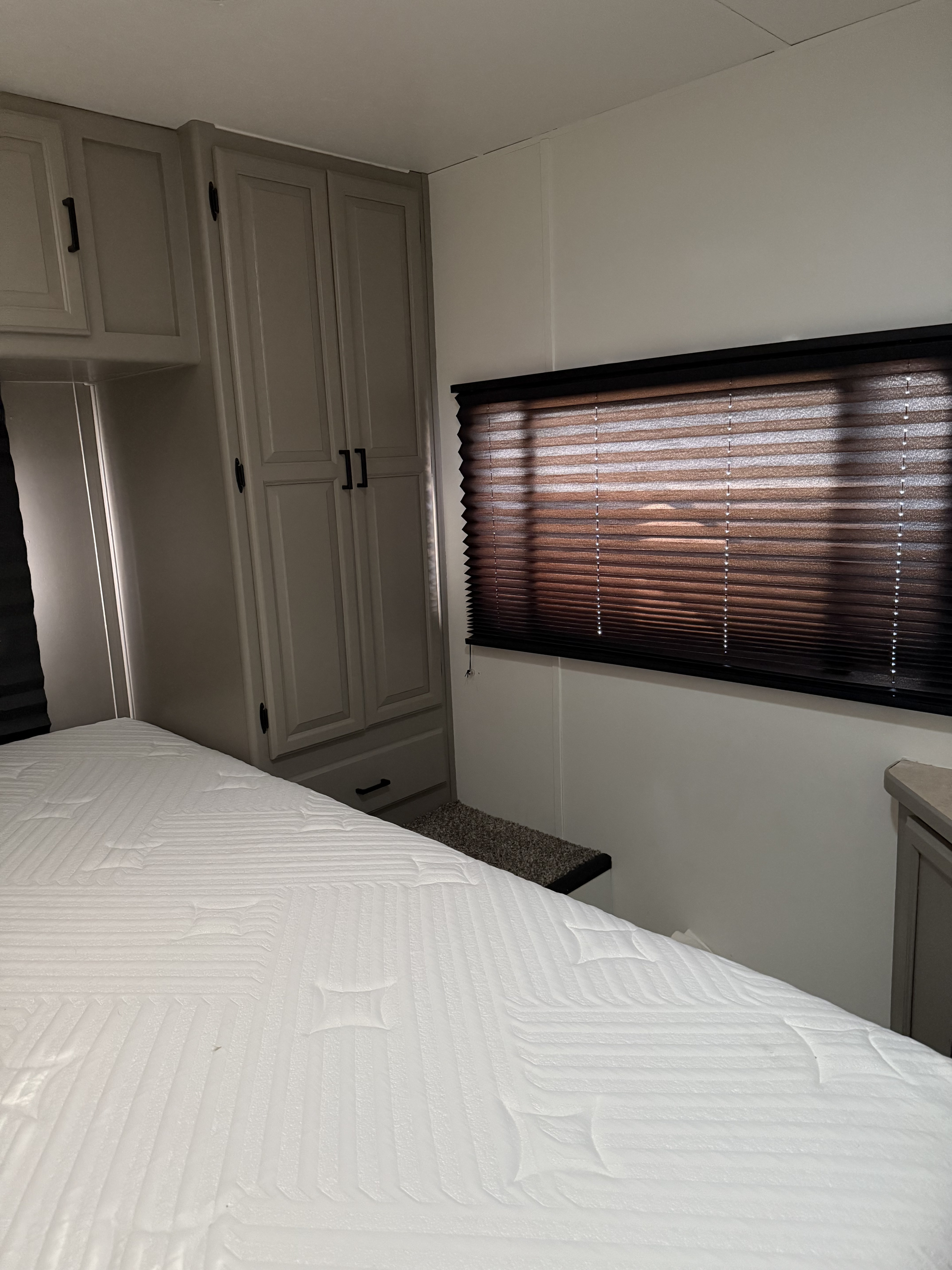 RV rental bedroom: white mattress, gray cabinets, and a dark pleated window blind. A compact and organized sleeping area.. Coachmen Leprechaun 2002