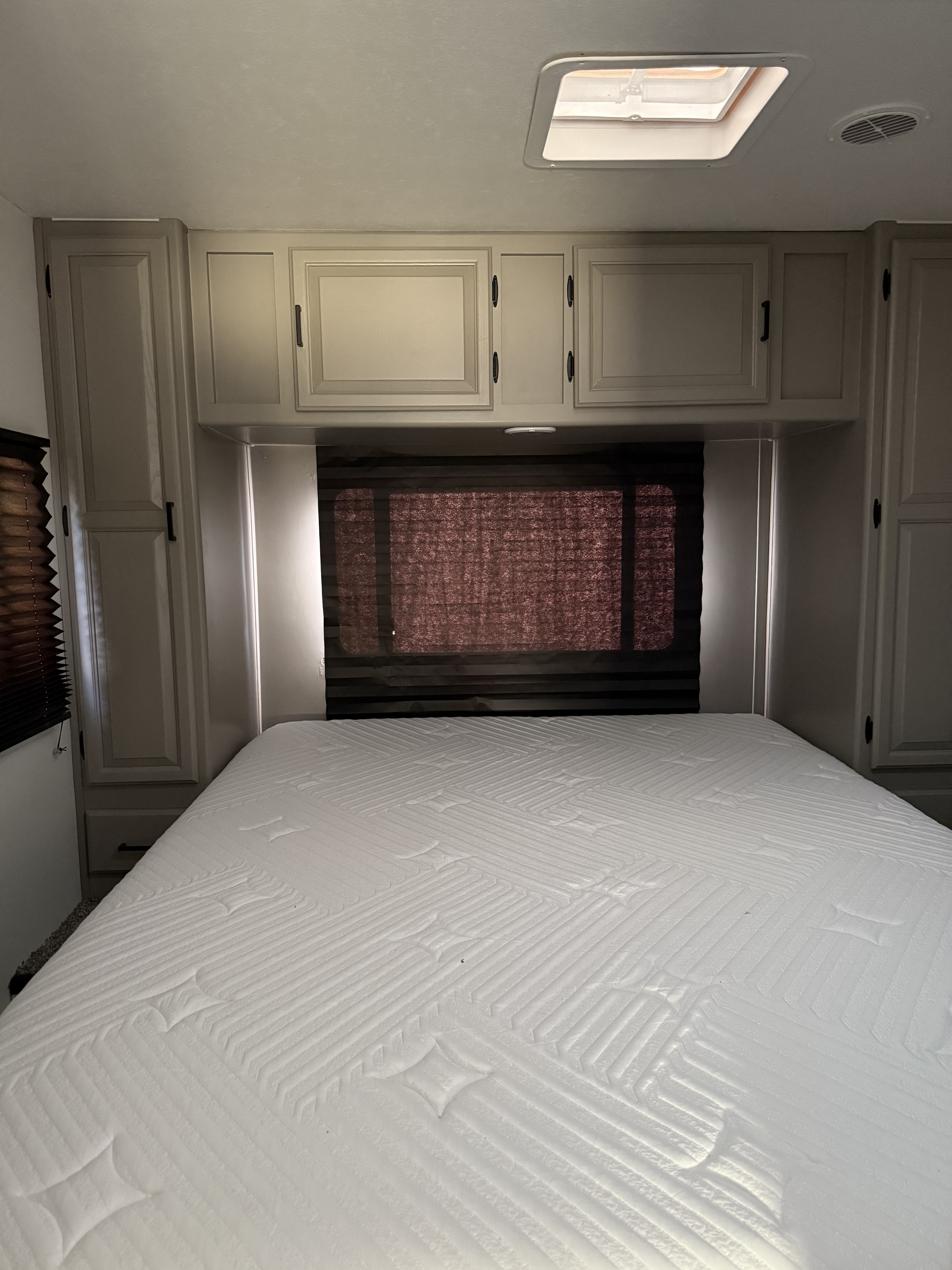 RV rental bedroom showing a large white mattress, wood cabinets, dark window blinds, and a ceiling skylight.. Coachmen Leprechaun 2002