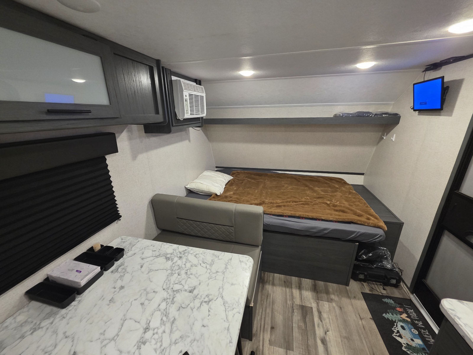 Well-appointed RV rental interior featuring a comfy bed, dinette, modern overhead cabinets, and window AC unit.. Dutchmen Aspen Trail 2023
