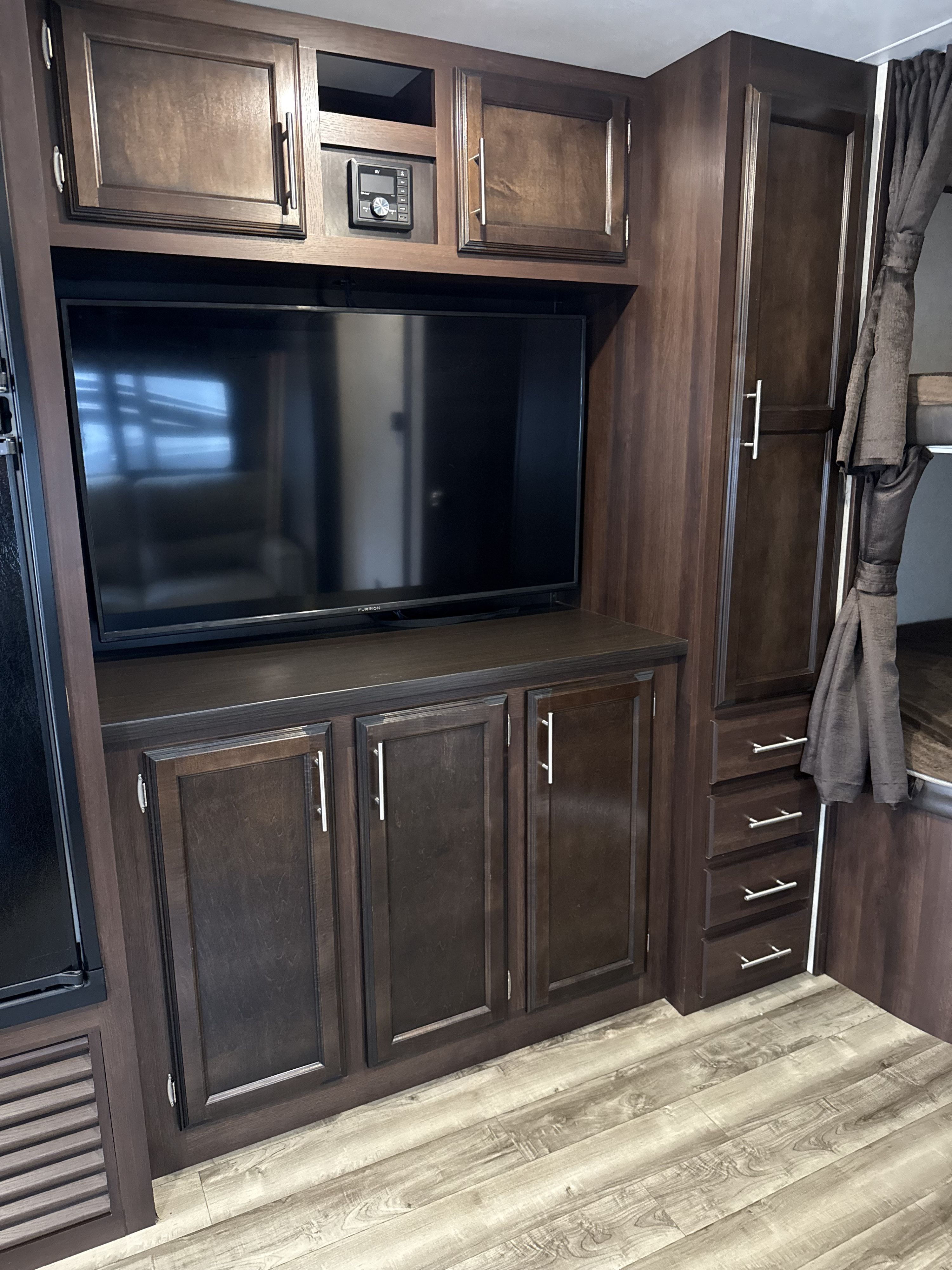 An RV rental's interior, featuring dark wood cabinetry, a TV, stereo, ample storage, and light wood-look flooring.. Jayco Jay Flight SLX 2019
