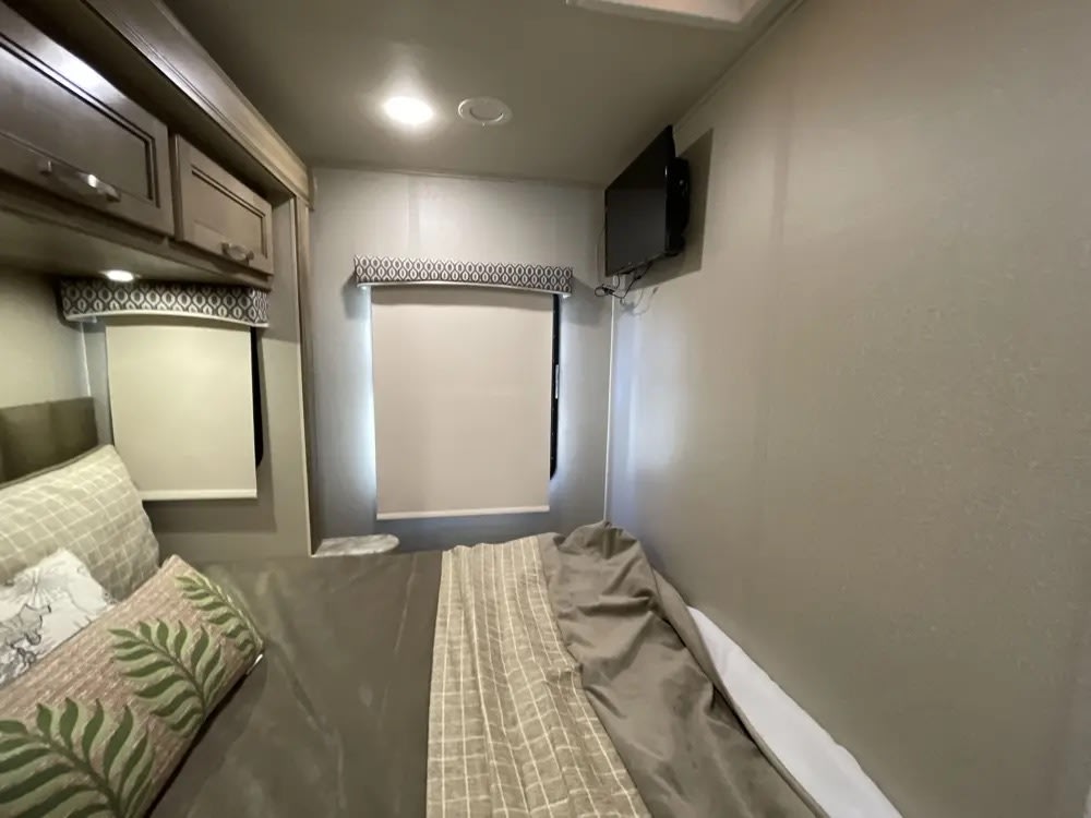 Cozy RV rental bedroom interior: soft bed with decorative pillows, overhead storage, roller window blinds, and a wall-mounted TV.. Entegra Coach Vision 2019