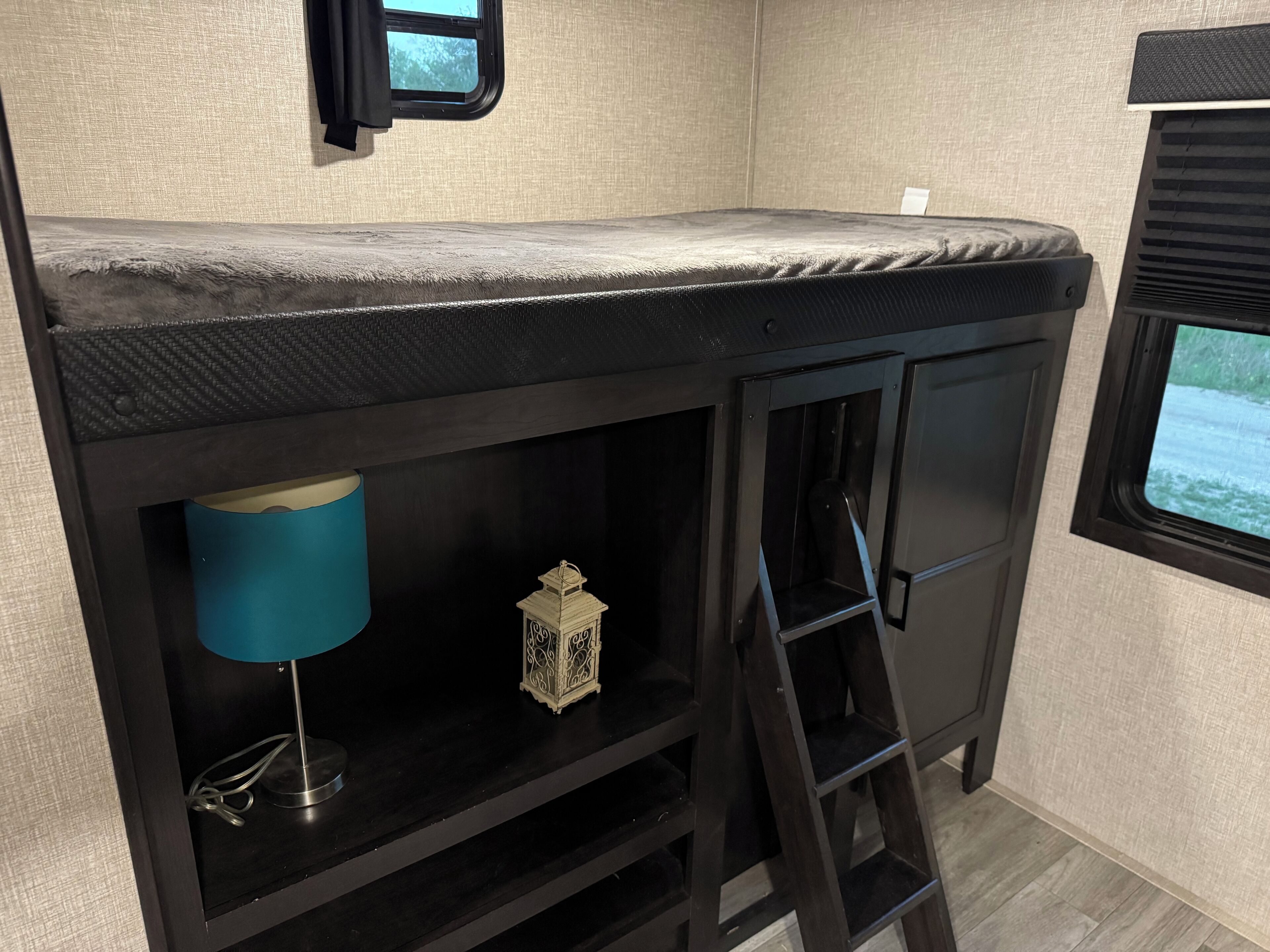 RV rental bunk bed with a plush gray mattress, integrated storage below, a ladder, and a blue lamp.. Jayco Jay Flight 2022