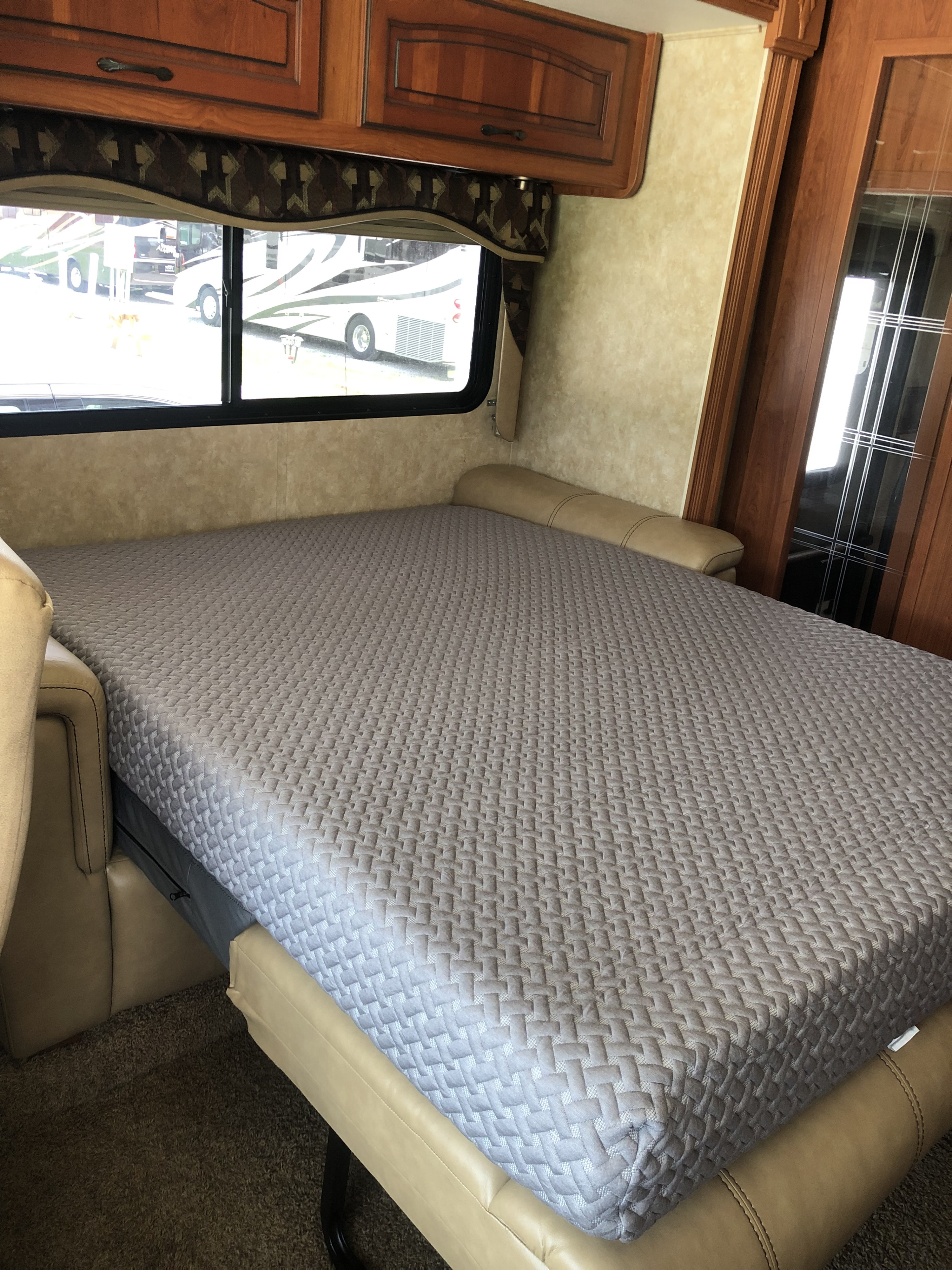 Inside an RV rental, a grey patterned mattress rests on a pull-out bed/sofa, framed by wooden cabinets and an outdoor view.. Forest River Coachmen Encounter 2011
