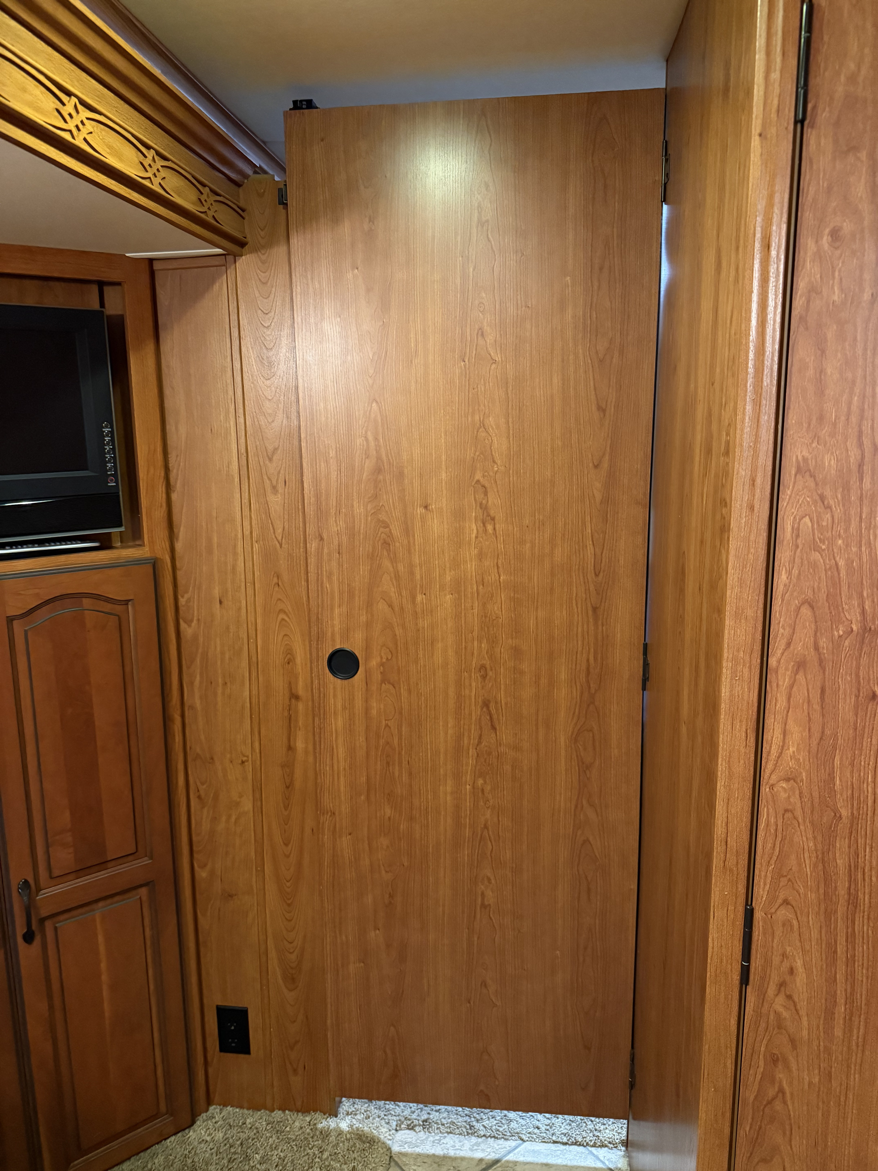Detailed view of an RV rental interior: rich wooden panels, a sliding door with a black handle, built-in TV, and decorative trim.. Forest River Coachmen Encounter 2011