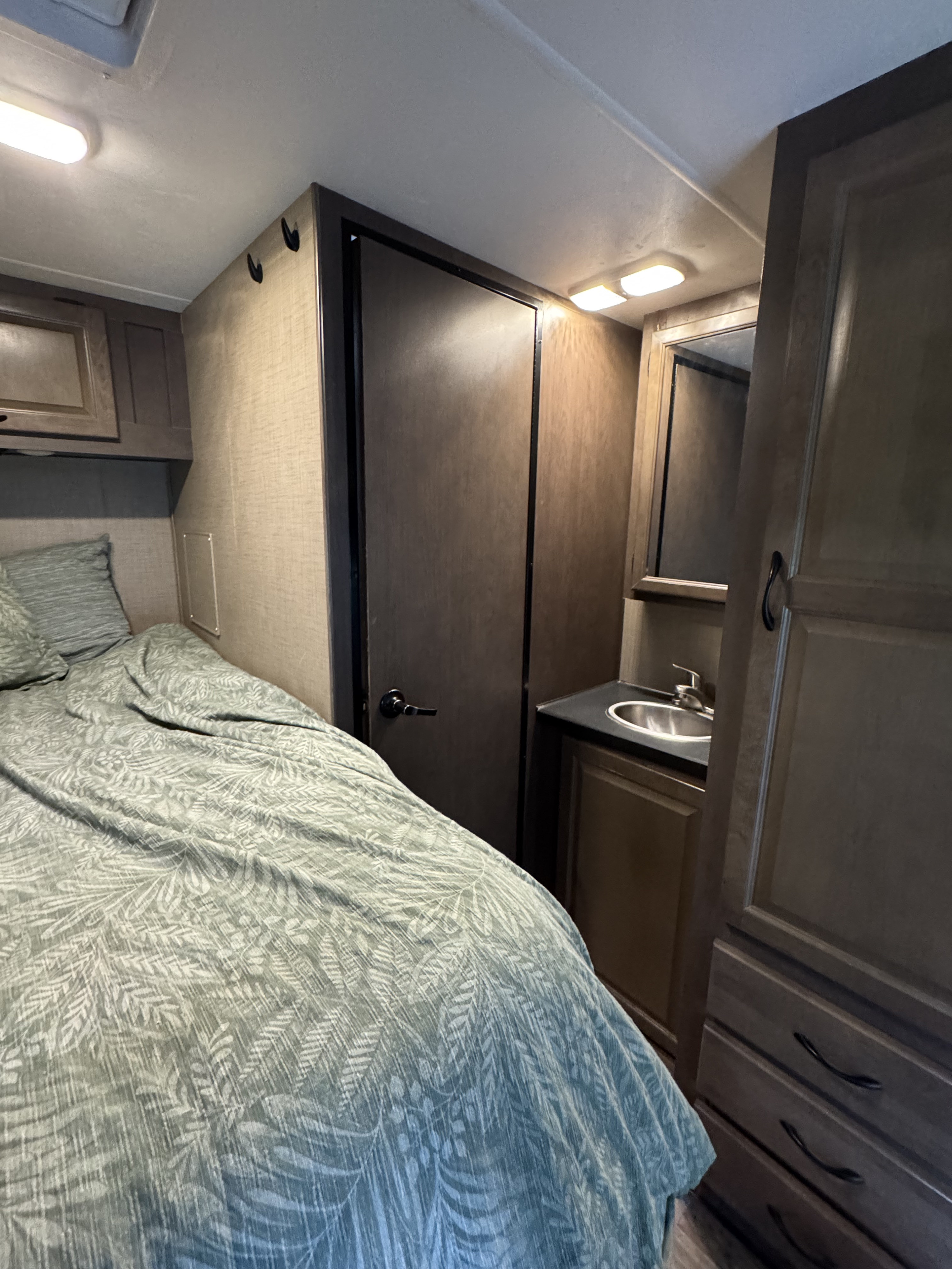 Inside an RV rental: Bed with leafy bedding, compact sink/vanity, and storage optimize small space.. Thor Majestic 2018
