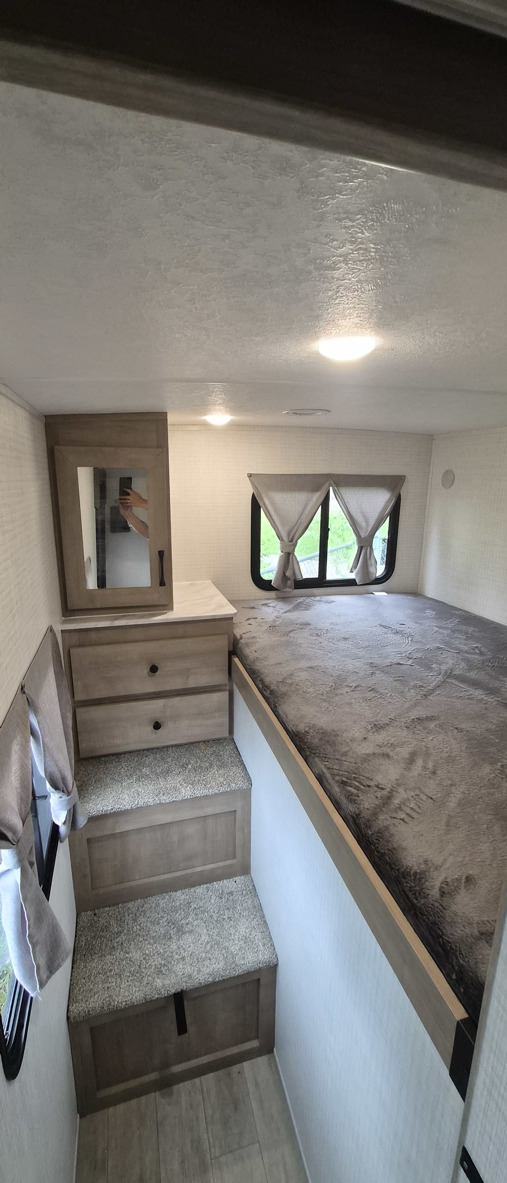 Cozy RV rental bedroom featuring a raised bed, steps with storage, and a mirrored cabinet for compact living.. Forest-river Solaire 3150 TBSS 2025