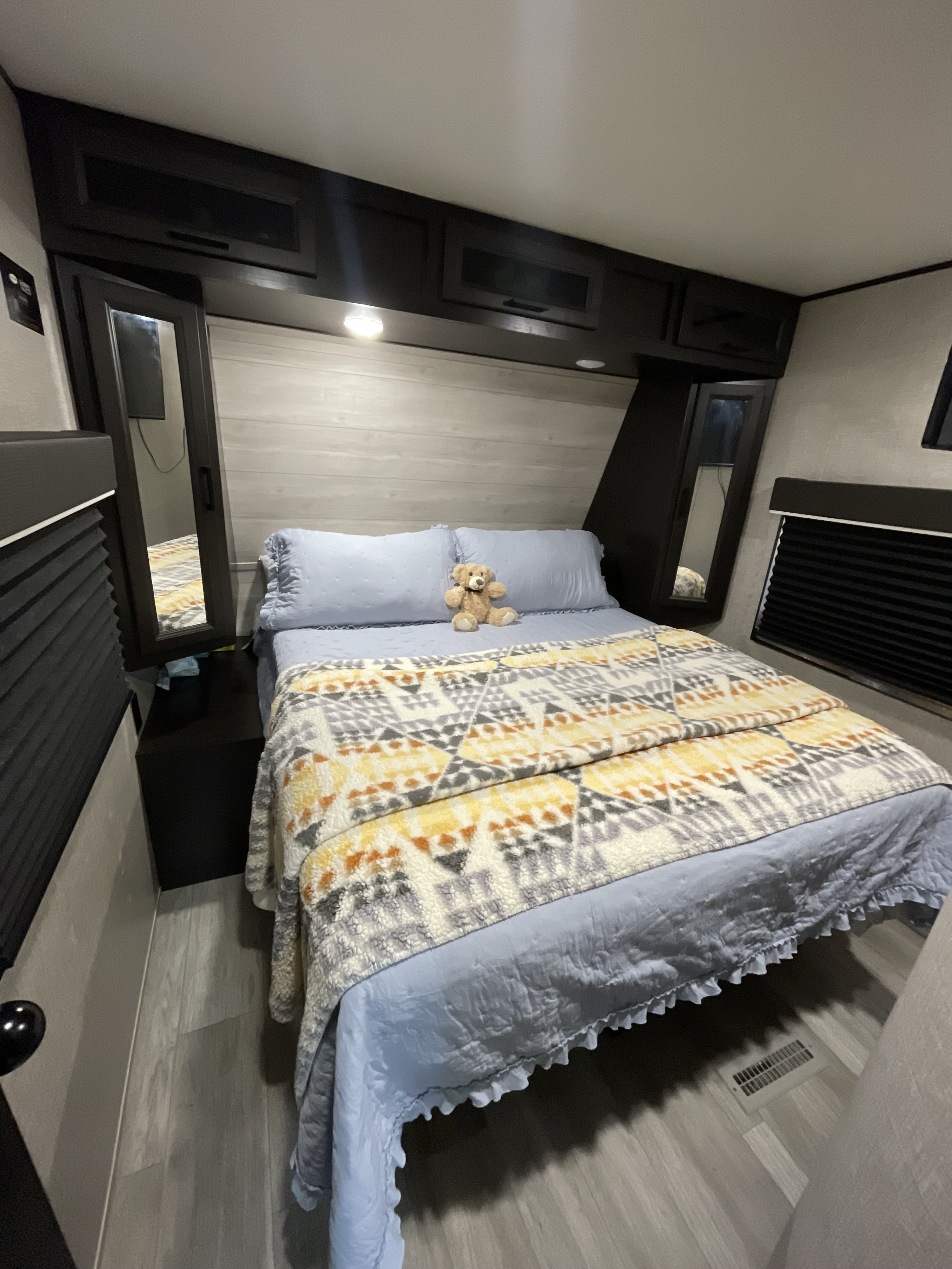 Cozy RV rental bedroom featuring a comfy bed, colorful blanket, teddy bear, overhead storage, and mirrored cabinets.. Jayco Jay Flight 2020