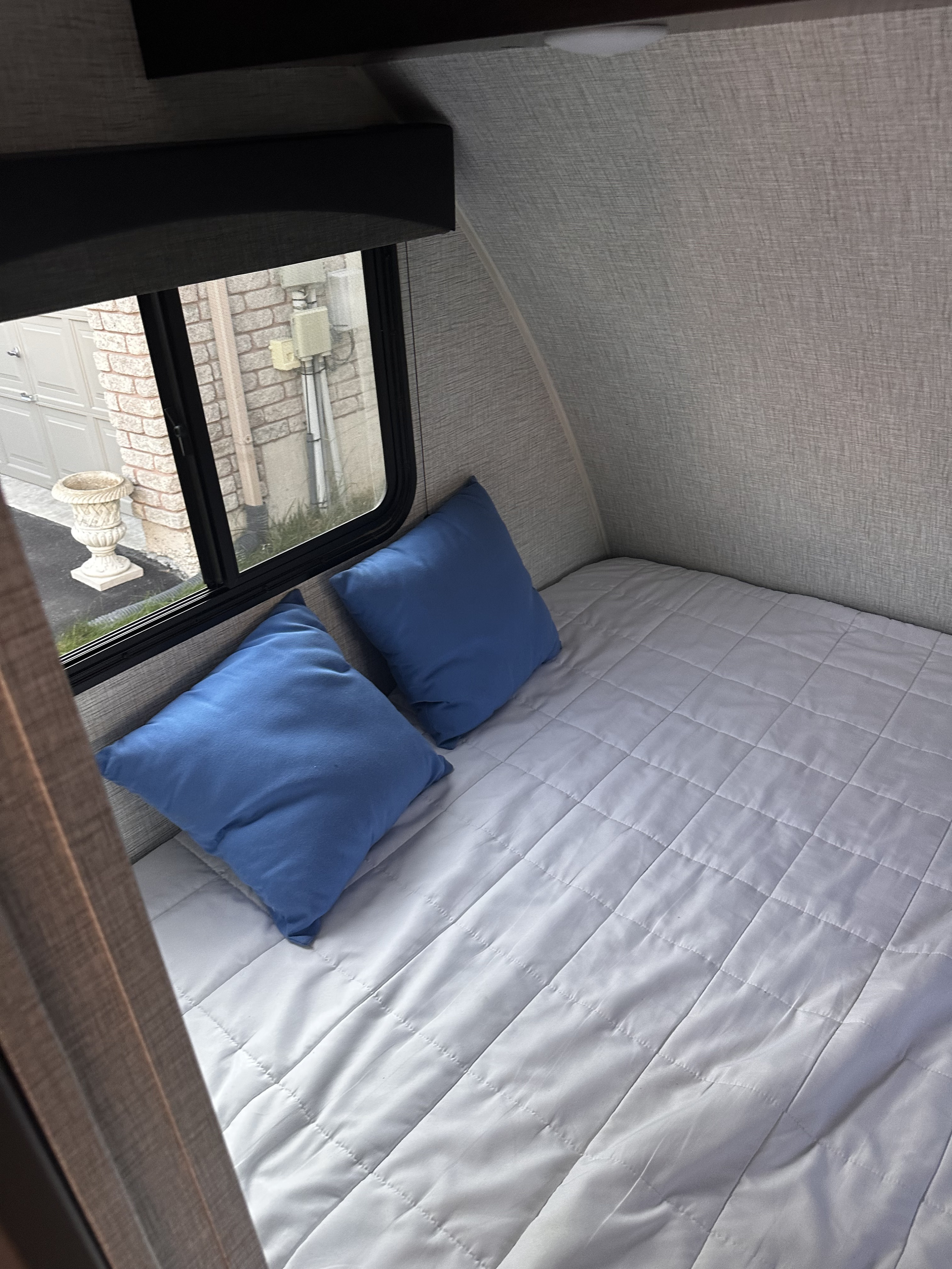 Experience comfort in this RV rental's cozy bed! Features blue pillows, quilted bedding, and a window view.. Braxton Creek Bushwhacker Plus 2022