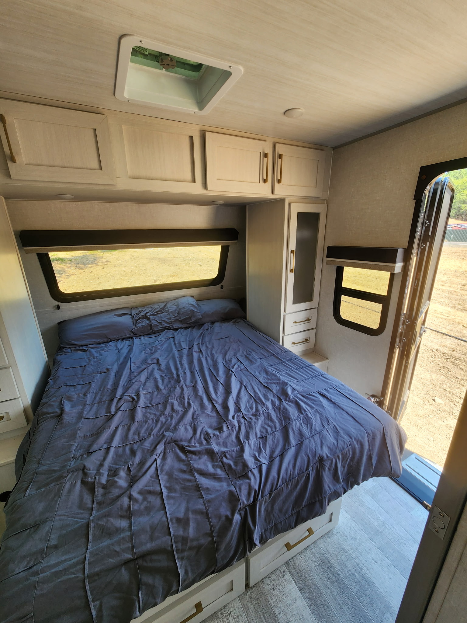 An RV rental bedroom showcasing a bed with dark blue bedding, light wood-toned cabinets, and windows providing outdoor views.. Forest River, INC NOBO 20.7 2025