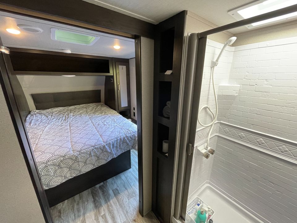 Inside an RV rental: a well-appointed bedroom with a skylight & a functional shower for travel comfort.. Grand Design Transcend Xplor 2021
