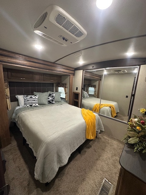 RV rental bedroom with a large bed, ceiling AC unit, built-in cabinets, and mirrored closet doors. Cozy, well-lit interior.. Keystone RV Laredo 2018