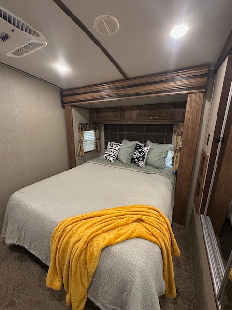 Cozy RV rental bedroom features a comfortable bed, yellow blanket, and built-in cabinetry.. Keystone RV Laredo 2018