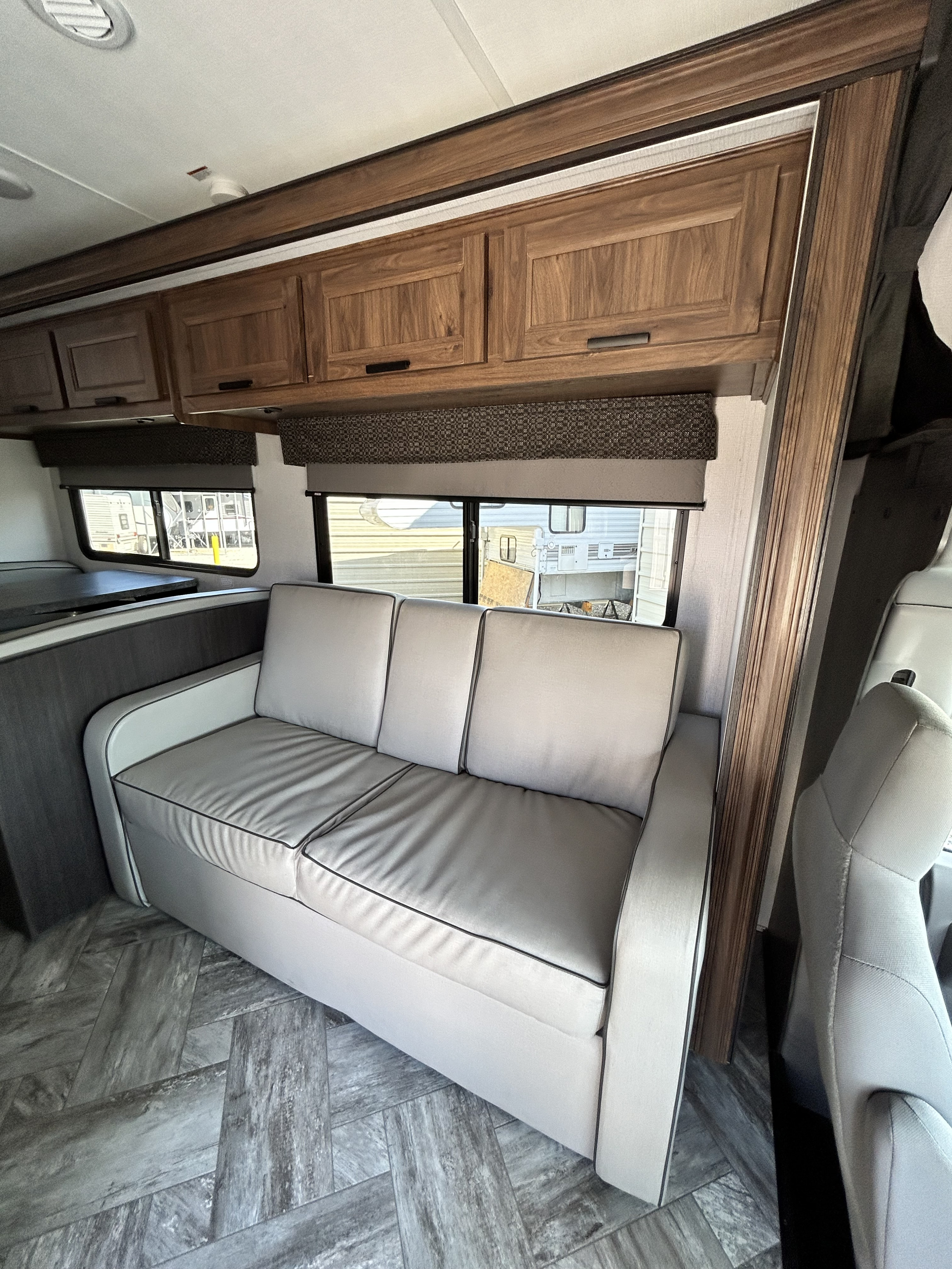 Inside an RV rental: a light gray sofa, wood cabinets, and large windows overlooking the outside. Herringbone flooring adds style.. Forest River Sunseeker LE 2022