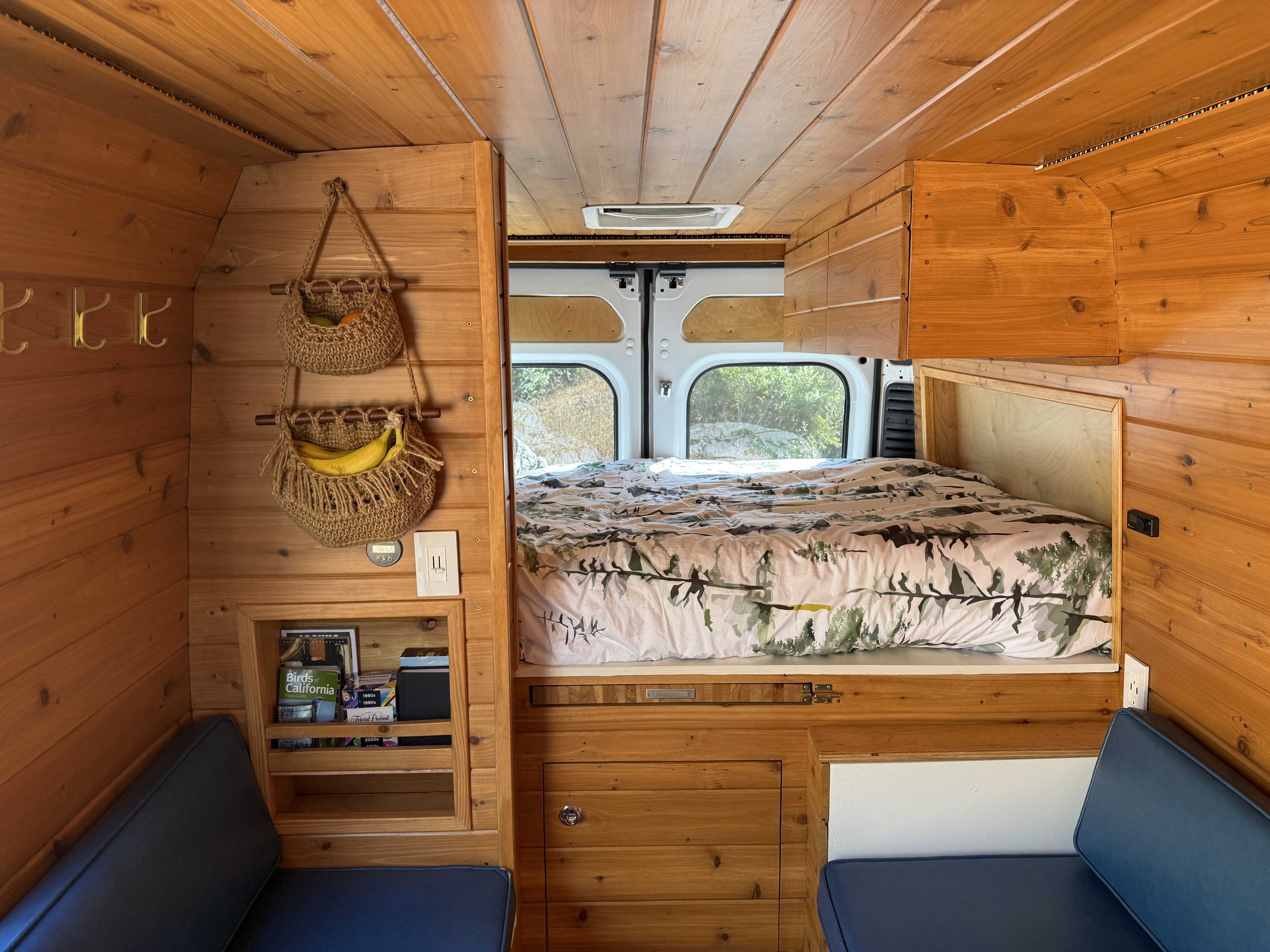 Inside an RV rental: a warm wood interior with a nature-themed bed, clever storage, and comfy blue seats.. RAM Promaster 2500 2020