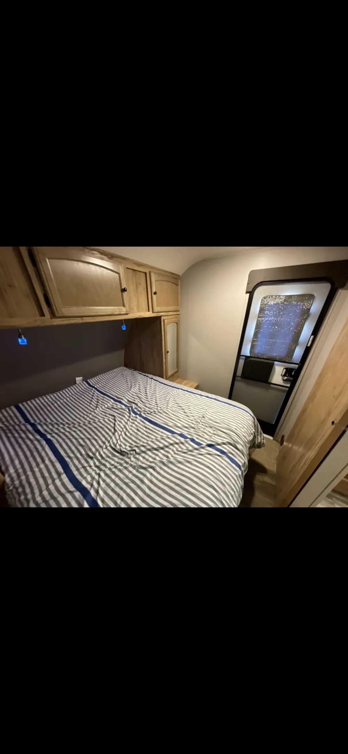 RV rental bedroom interior: striped bed, wood cabinets, and door. Cozy space for your next adventure.. Coachmen Apex LE 2018