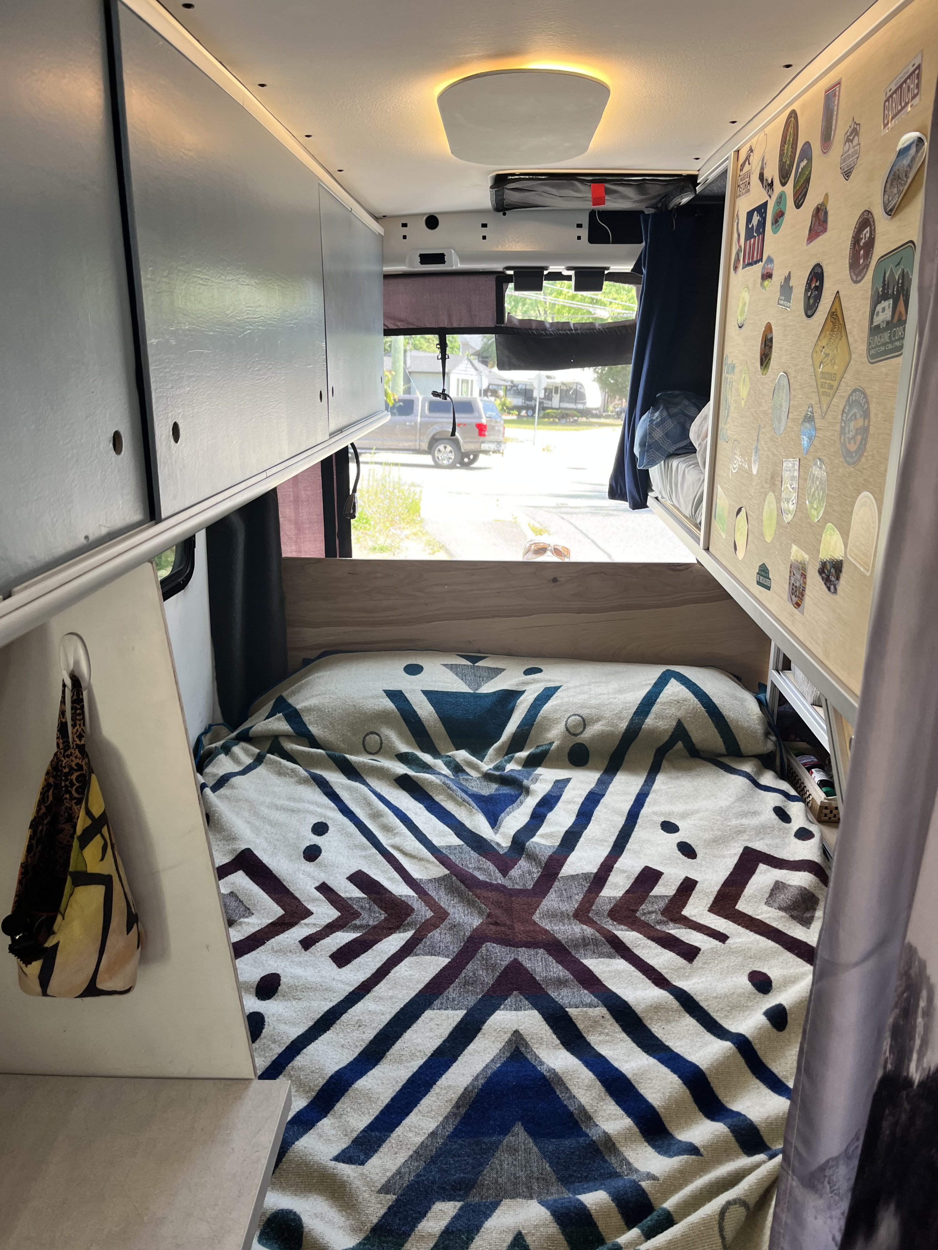 Inside a comfy RV rental camper, showcasing a geometrically patterned bed, overhead storage, and a travel sticker wall.. Ford Transit 350 2021