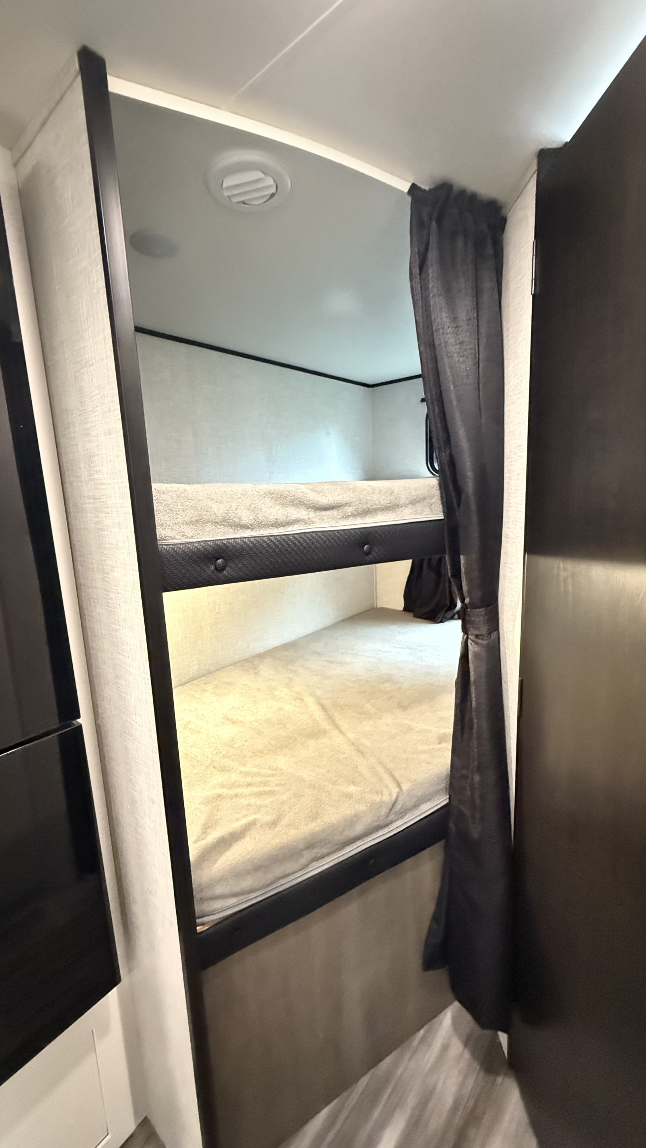 Interior view of an RV rental showing stacked bunk beds with mattresses & privacy curtain for comfortable sleeping.. jayco 235MBH Jay Flight TT 2025