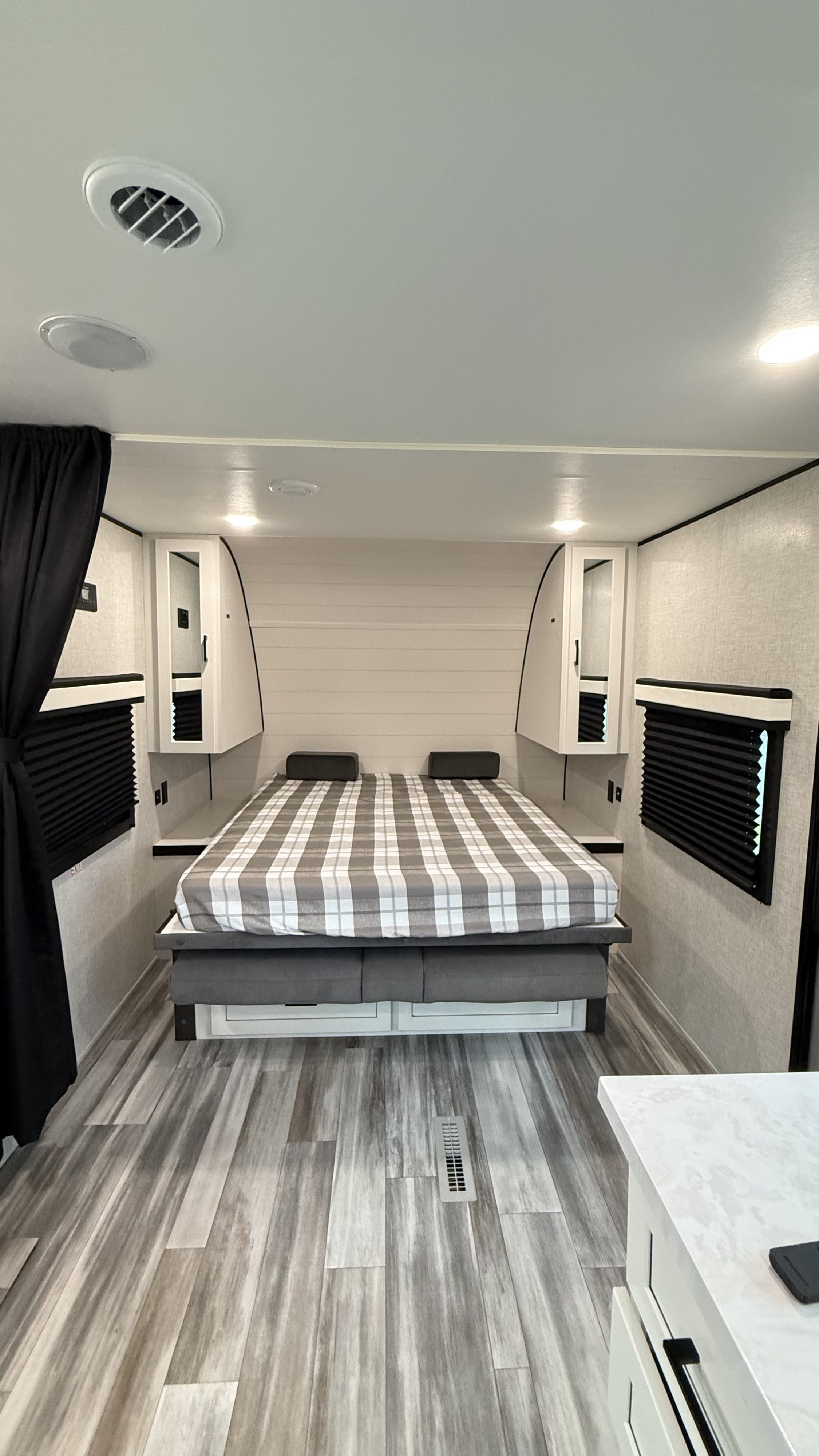 RV rental bedroom shows a bed with plaid bedding, overhead cabinets, window blinds, and wood-look flooring.. jayco 235MBH Jay Flight TT 2025