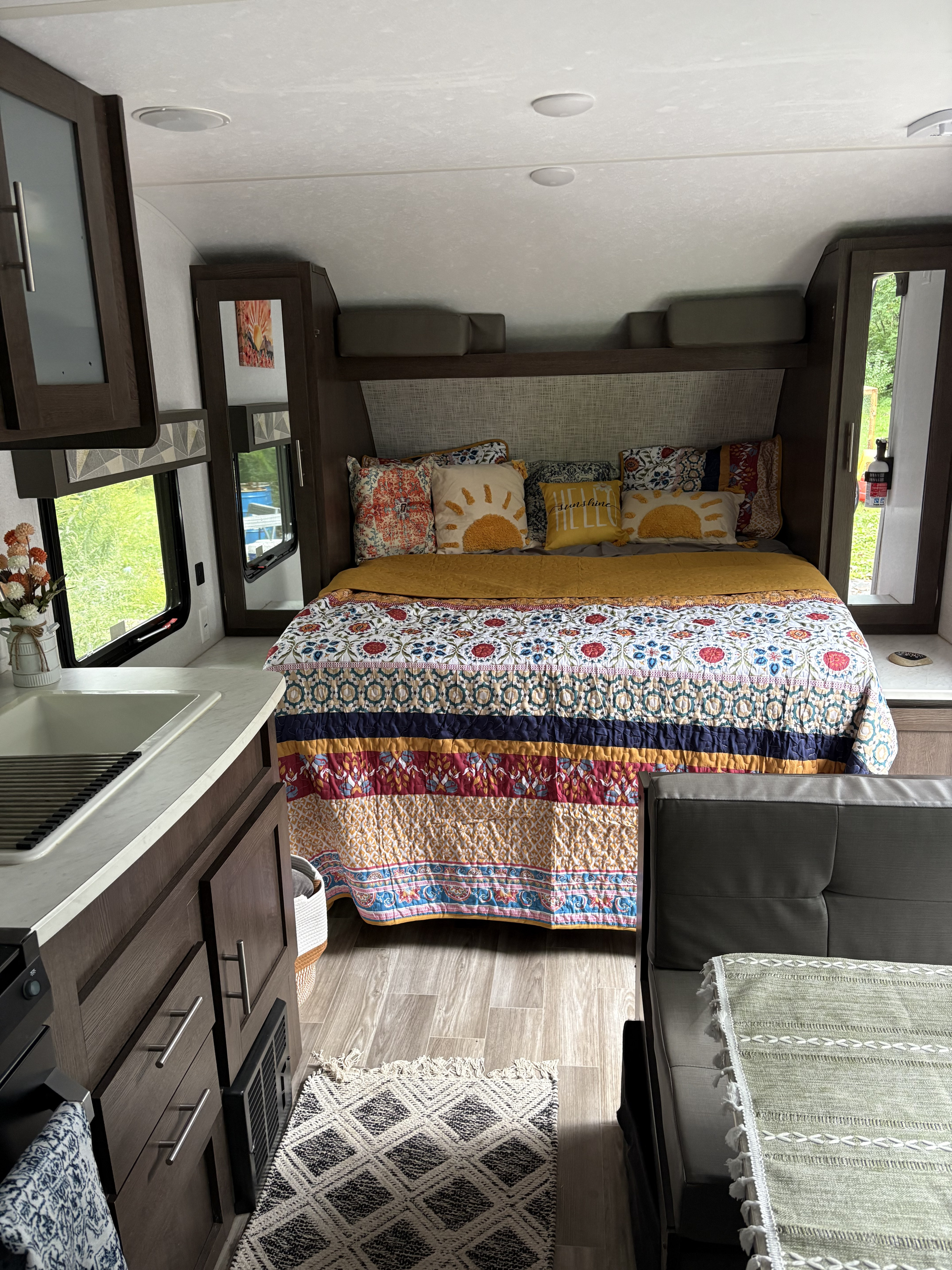 Colorful RV rental interior: a comfy bedroom with sunny pillows & a vibrant quilt, next to the kitchen sink.. Forest River Wildwood X-Lite 2019
