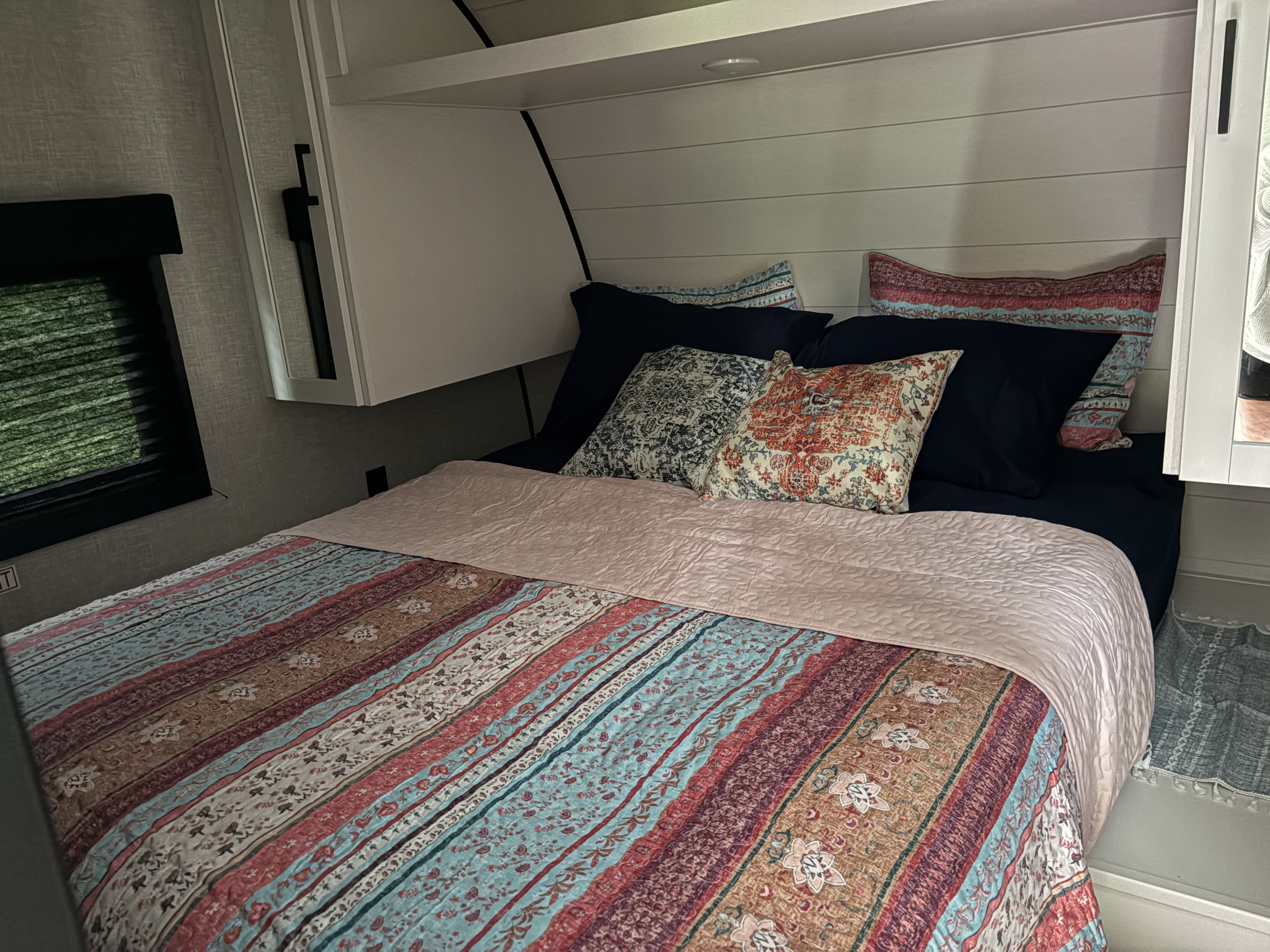 Colorful bedding on a comfortable bed inside an RV rental bedroom, featuring overhead storage and a window view.. Open Range Open Range 2026