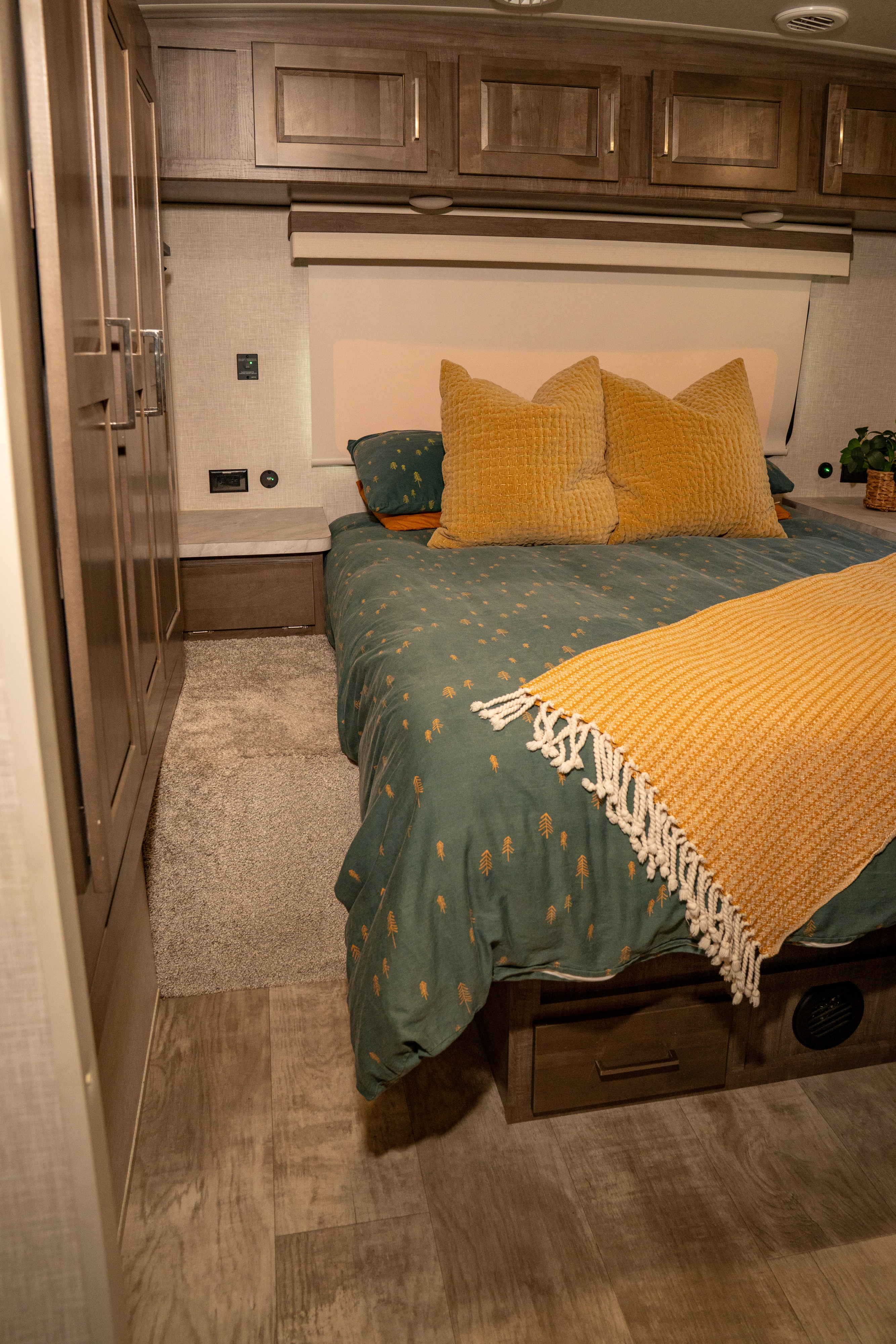 Cozy bedroom in an RV rental, featuring green bedding with tree patterns, yellow accents, and overhead storage. Ideal for travel.. Forest River Rockwood Ultra Lite 2023