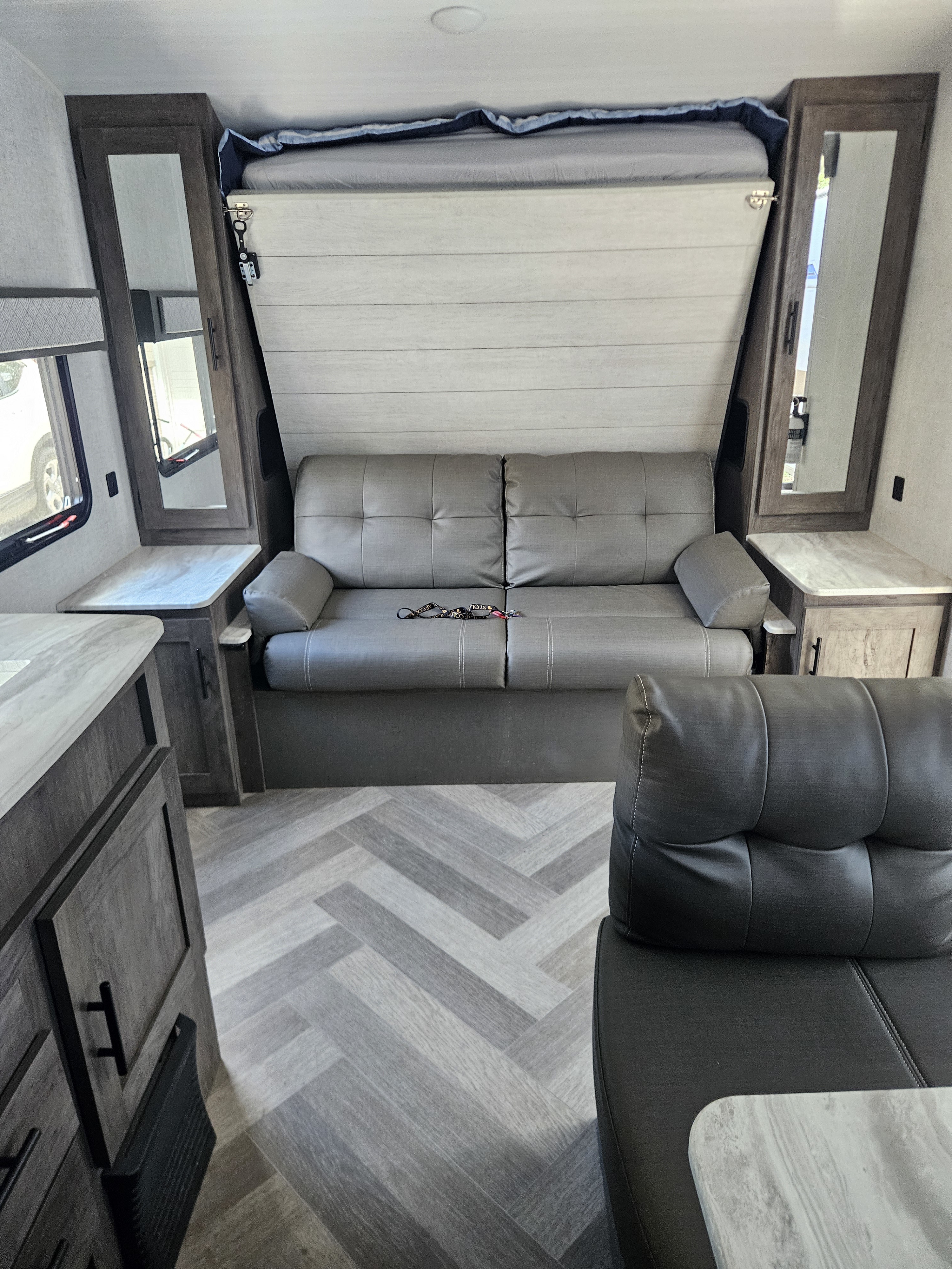 RV rental interior: A comfy grey sofa, stowed bed, modern wood cabinets, and herringbone floor. Perfect compact living space.. Forest River Salem Cruise Lite 2020
