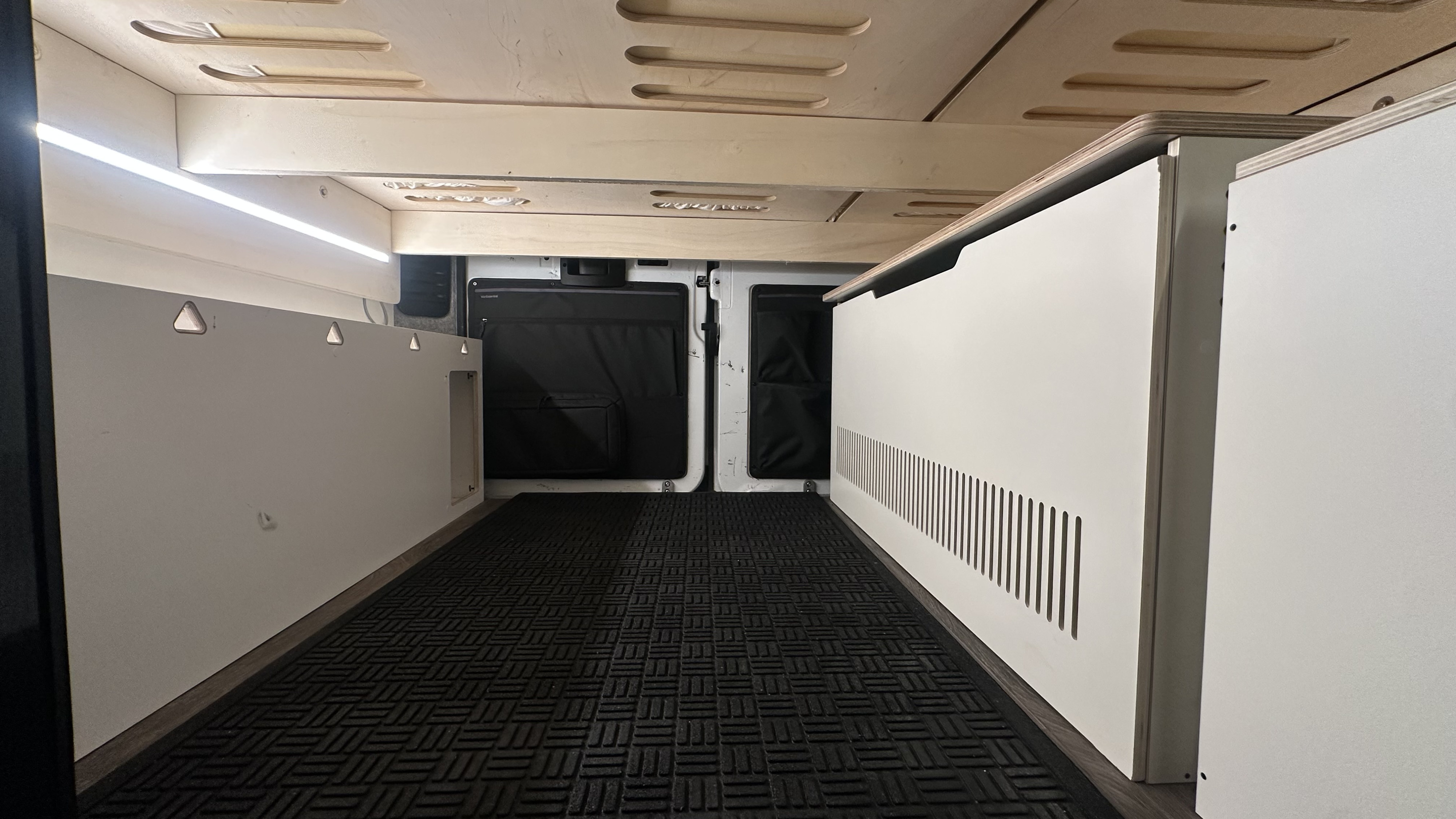 RV rental's rear interior cargo space. Features modular bed platform, bright LED lights, and sturdy floor mat.. Ram Promaster 2500 2023