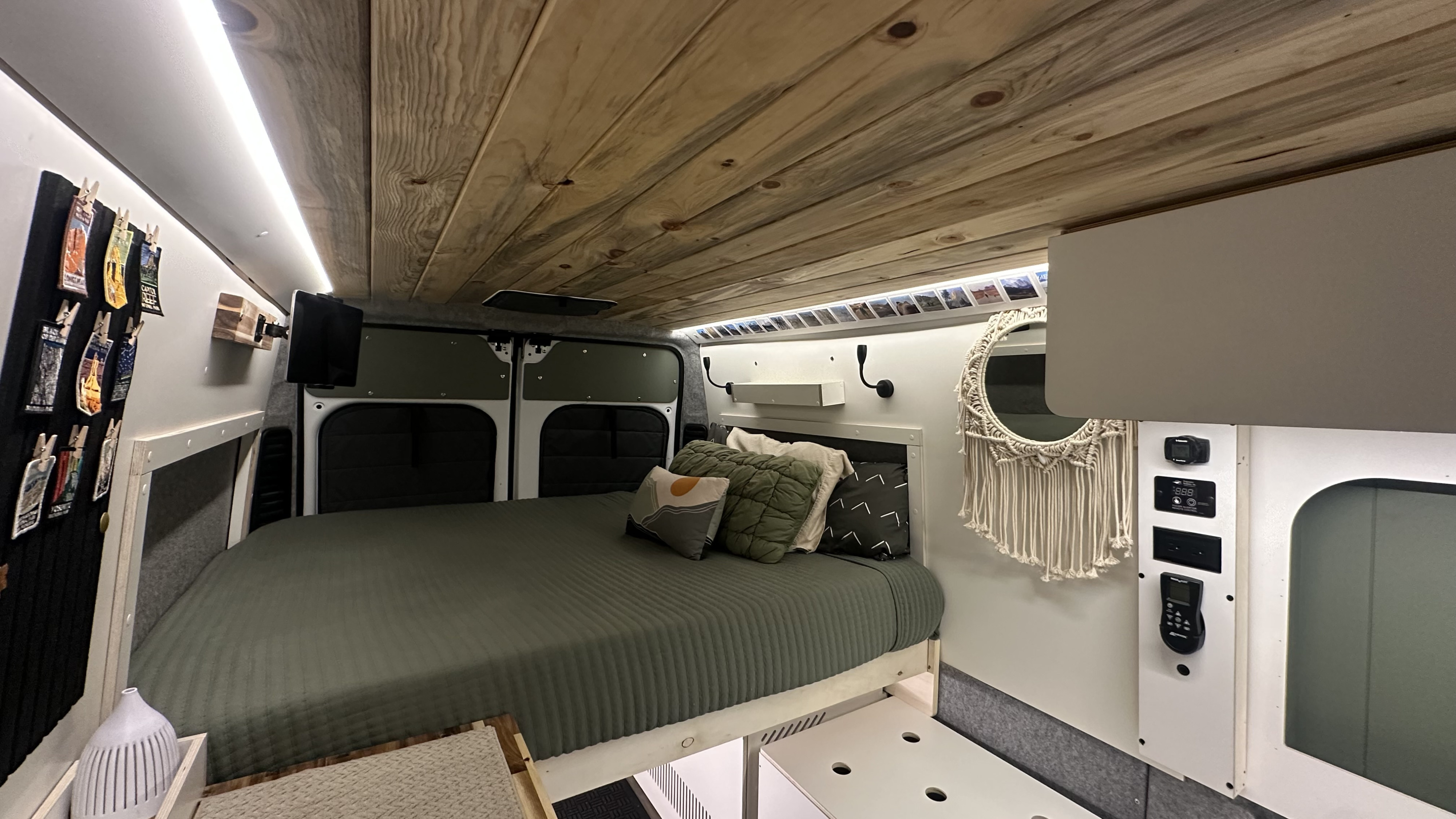 Inside a stylish RV rental, featuring a comfortable bed, wood ceiling, LED lighting, and essential controls for van life adventures.. Ram Promaster 2500 2023