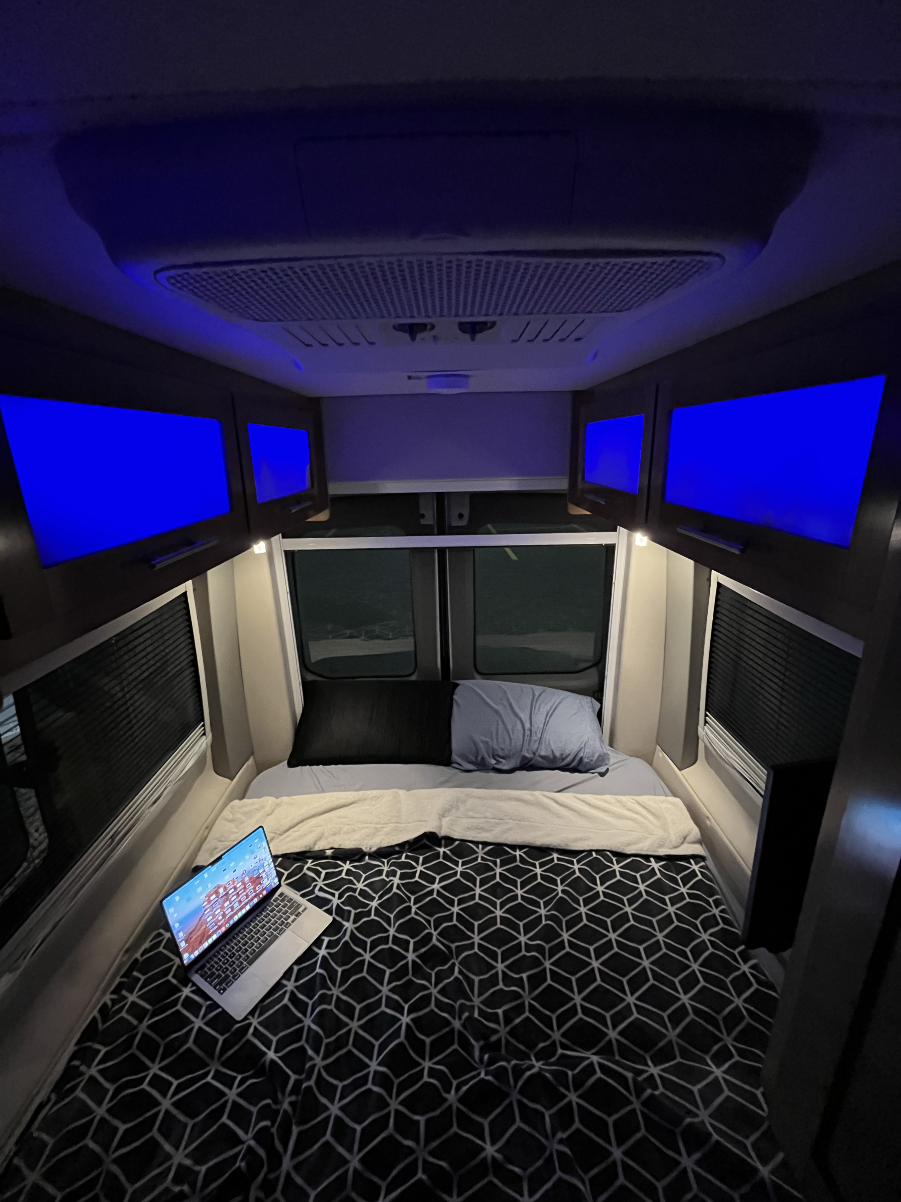 Inside an RV rental: a cozy bedroom setup with a laptop, bright blue screens, and patterned bedding.. Coachmen Beyond 2020