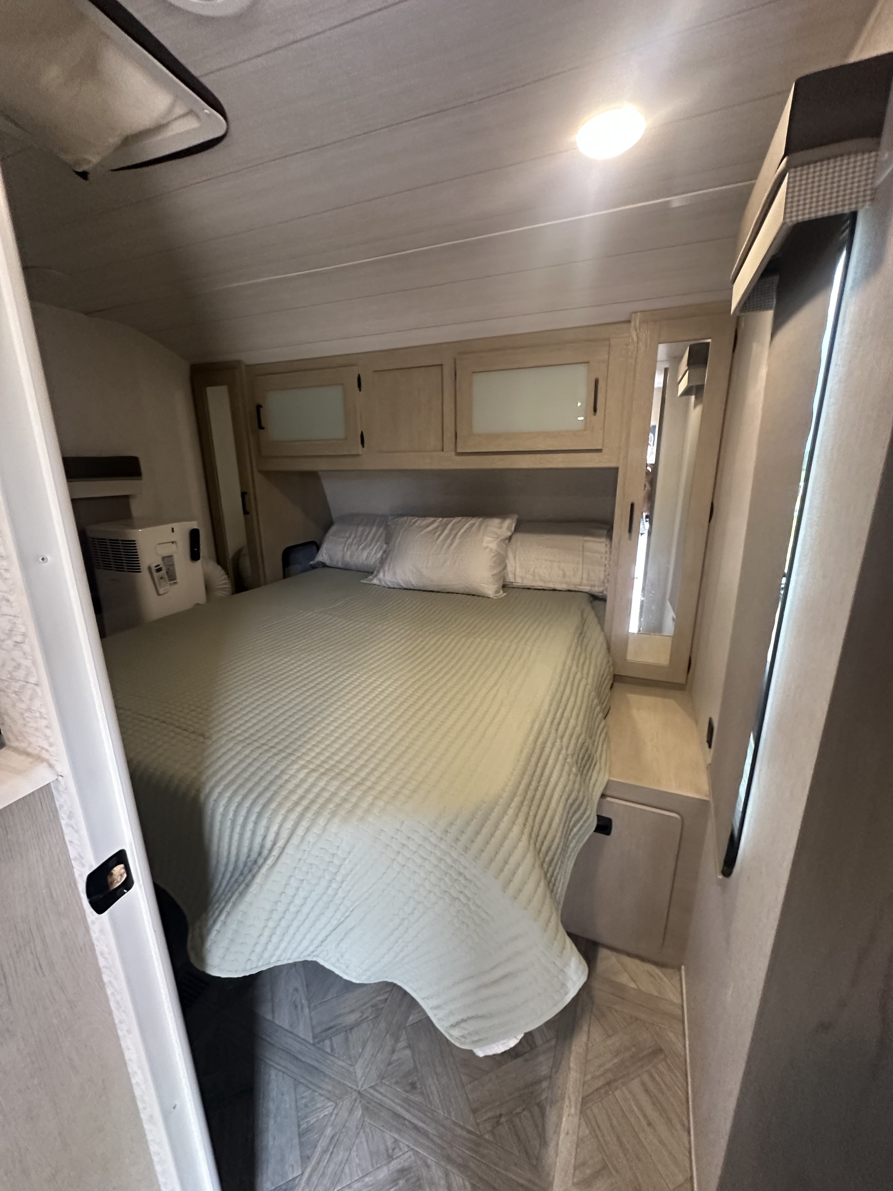 Cozy RV rental bedroom with a comfortable bed, built-in storage, and AC unit. Enjoy compact comfort on your travels.. Forest River Wildwood 2023